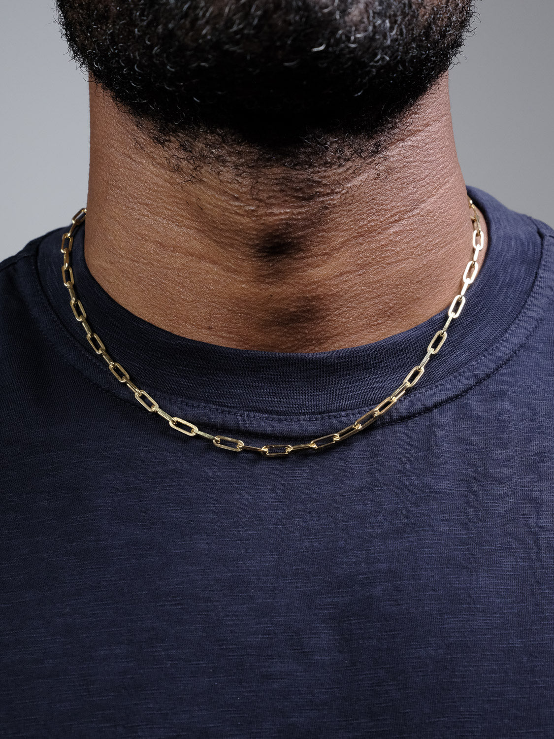 A close-up of a person wearing the Kai 120 Paper Clip Chain Necklace by ID Menswear over a dark navy t-shirt, with focus on their neck and lower face.