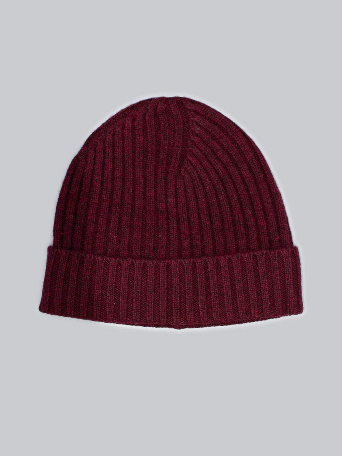 The Kailash Merino Wool Beanie by ID Menswear, crafted from Merino wool, is a maroon ribbed knit with a folded cuff. It sits on a light gray background and offers warmth and softness, ideal for outdoor adventures.