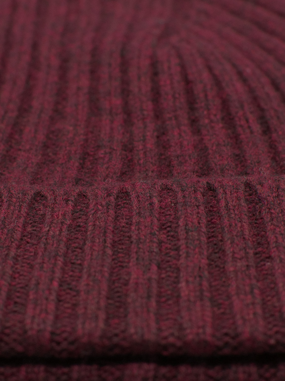 Close-up of a ribbed, maroon knit textile highlighting detailed texture and stitching, embodying the warmth and softness ideal for outdoor adventures with the Kailash Merino Wool Beanie by ID Menswear.