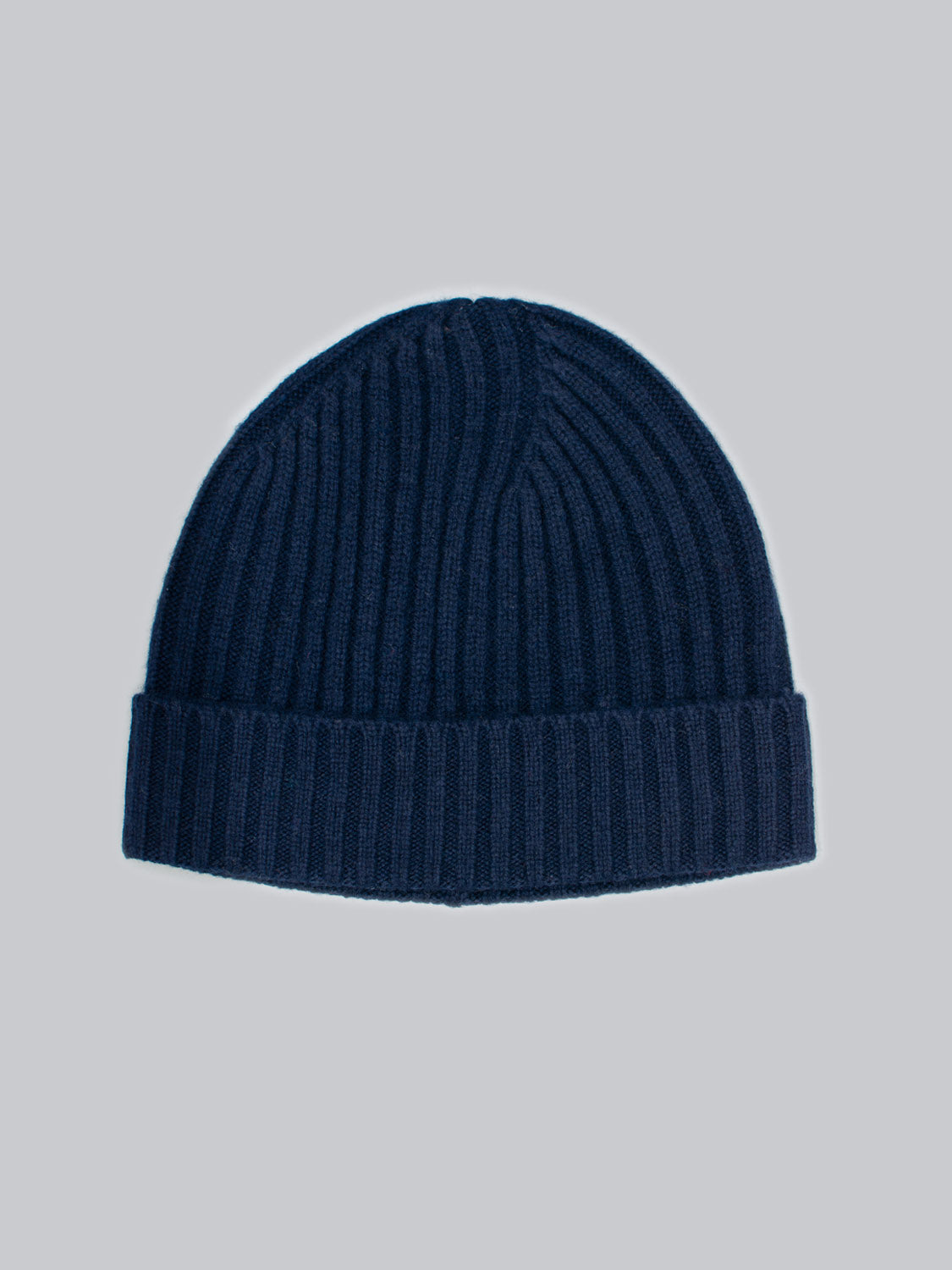 The Kailash Merino Wool Beanie by ID Menswear is a navy blue, ribbed hat with a folded cuff, providing warmth and softness for outdoor adventures, shown against a light gray background.