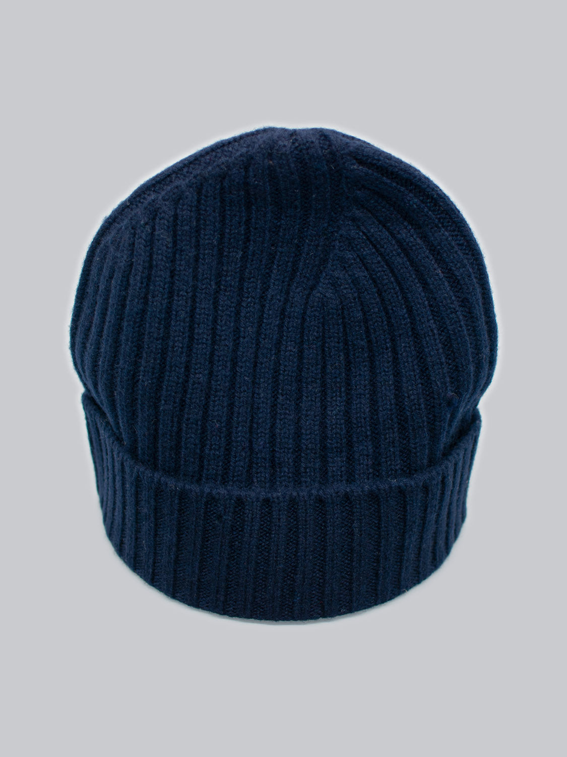 Experience the warmth and softness of ID Menswears Kailash Merino Wool Beanie, featuring a ribbed navy blue knit with a folded brim against a light gray backdrop. Perfect for outdoor adventures, this luxurious beanie is crafted from merino wool.