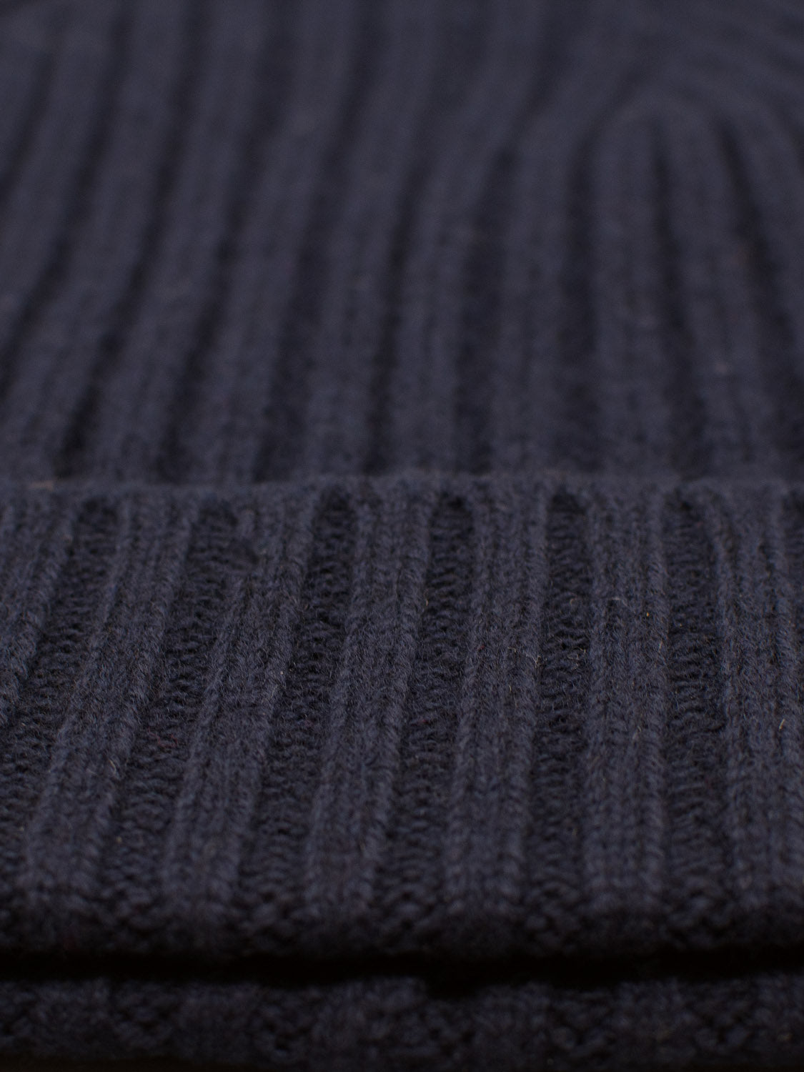 Close-up of ID Menswears Kailash Merino Wool Beanie dark knitted fabric with vertical ribbed texture, highlighting intricate details and pattern for warmth and softness.