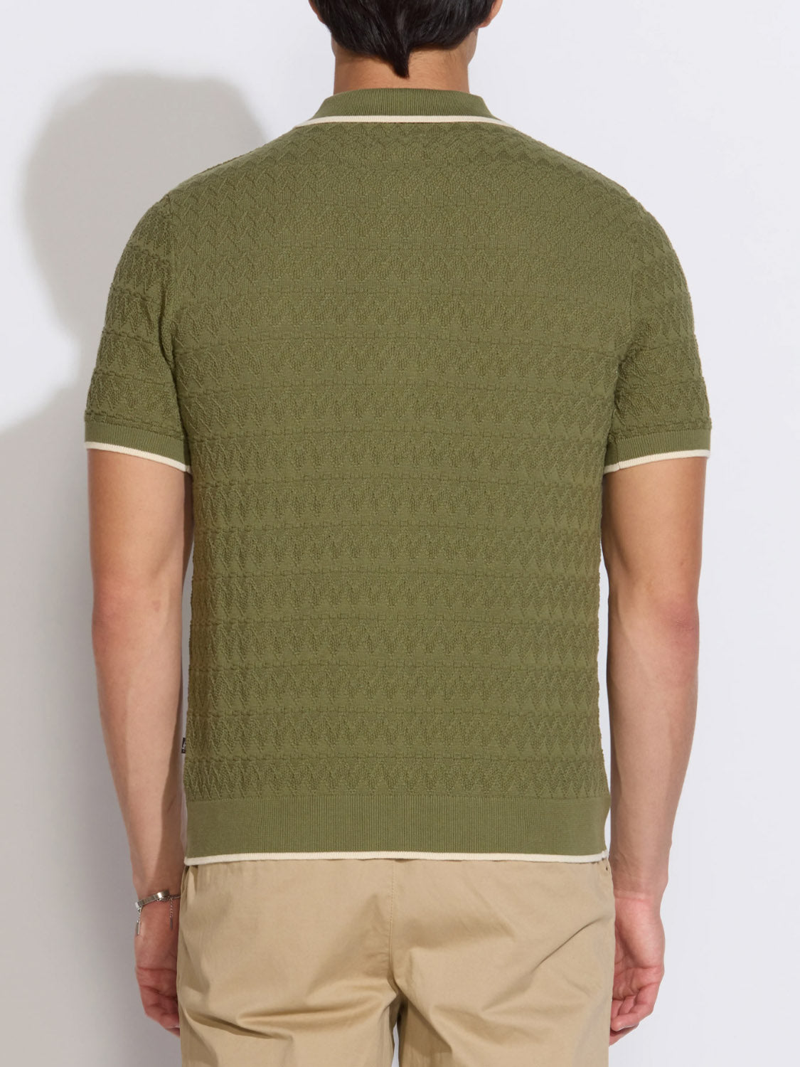 A man is seen from the back in the Civil Society Kalino Full Placket Sweater Polo—an olive green textured knit with cream trim on the sleeves, collar, and hem—styled with beige pants for a modern men's fashion look.