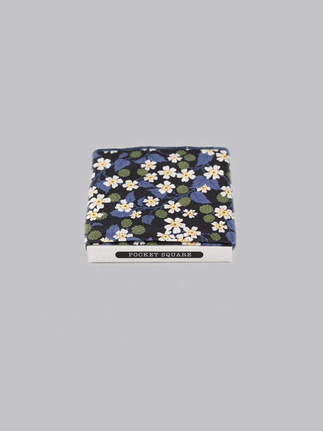 A folded Liberty™ Karen Pocket Square by ID Menswear, featuring a blue background with white and yellow floral patterns, is displayed in a white box labeled POCKET SQUARE on a plain gray background.