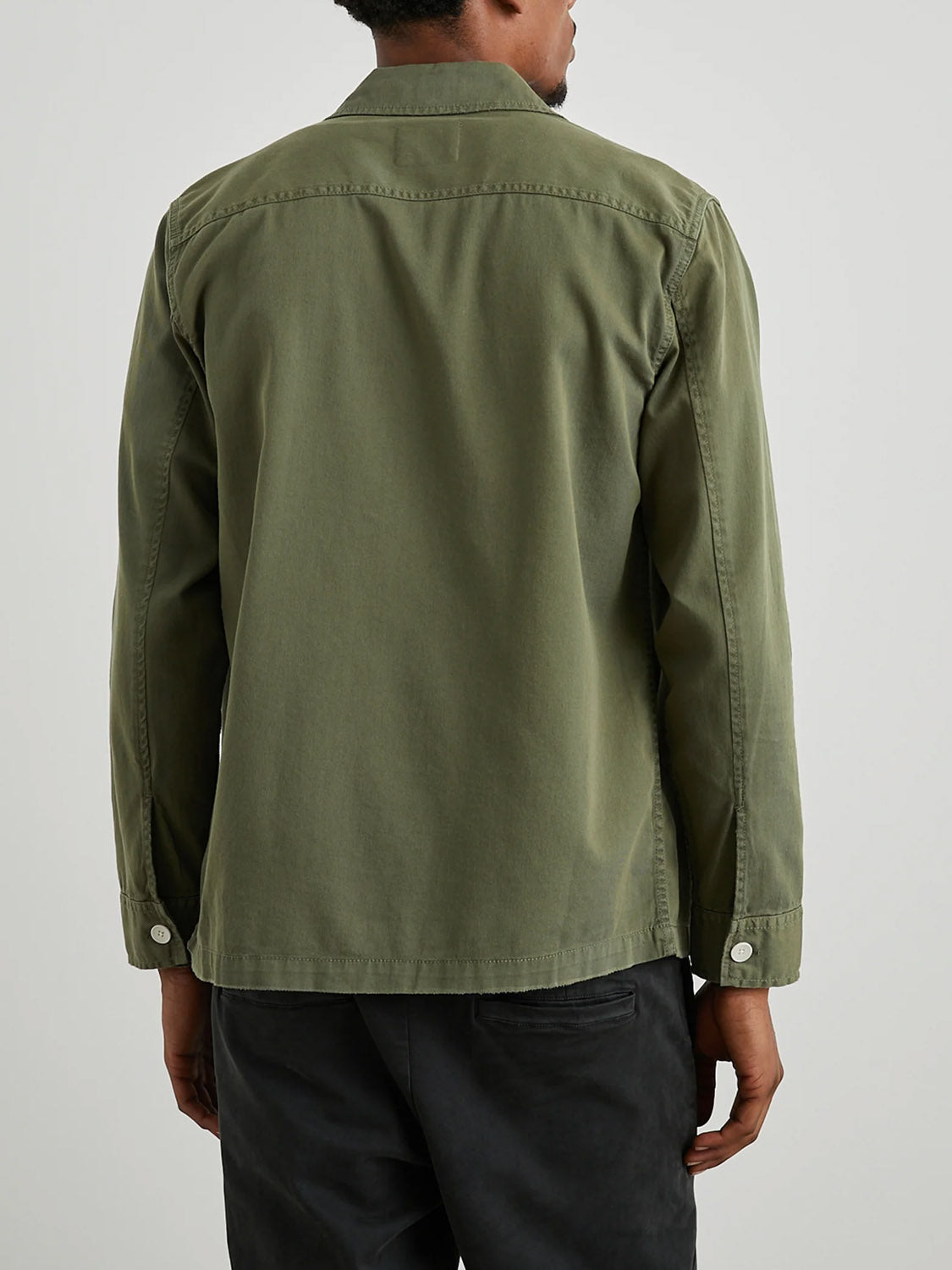 A person is wearing a Rails Kerouac Shirt Jacket by Rails in a classic green military style with cotton twill texture. They have short hair and are facing away, paired with dark pants against a light-colored background.