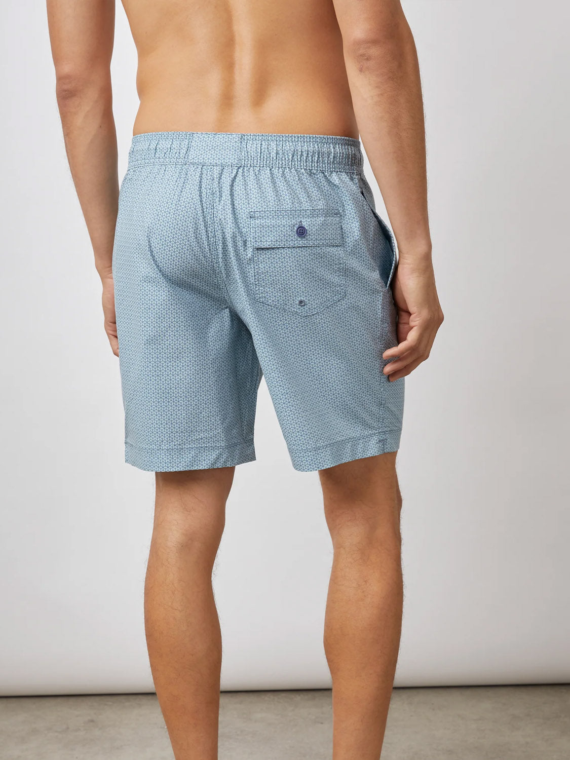 Wearing Rails lightweight cotton-blend Kian Swim Short in a light blue pattern with a back pocket, a person faces away from a plain, light wall, showcasing the effortless style of these trunks with an uncovered upper body.