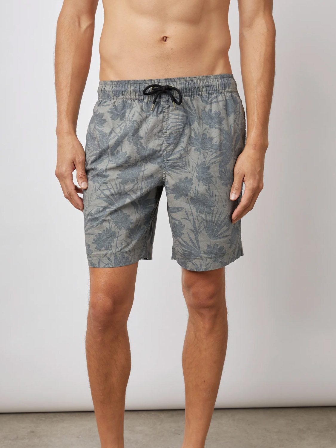 A man stands against a plain background wearing Rails Kian Swim Short. The cotton-blend trunks feature a subtle leaf pattern with a black drawstring at the waist, and his arms rest by his sides for a relaxed look.