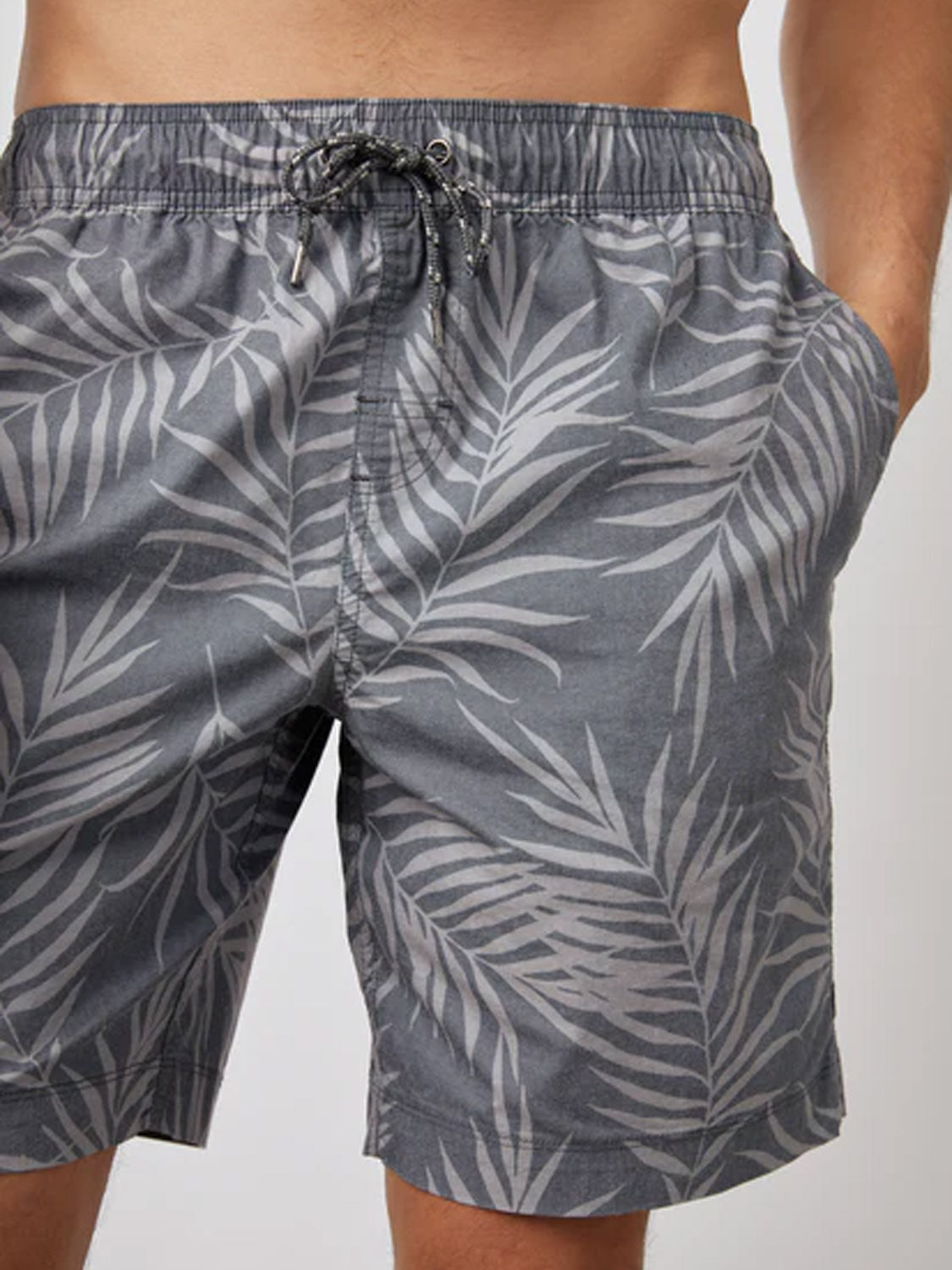 Someone is wearing Rails Kian Swim Short in grey with a white palm leaf pattern, made from a lightweight cotton blend. The trunks feature an elastic waistband with drawstring and side pockets, while their upper body is partially out of view.