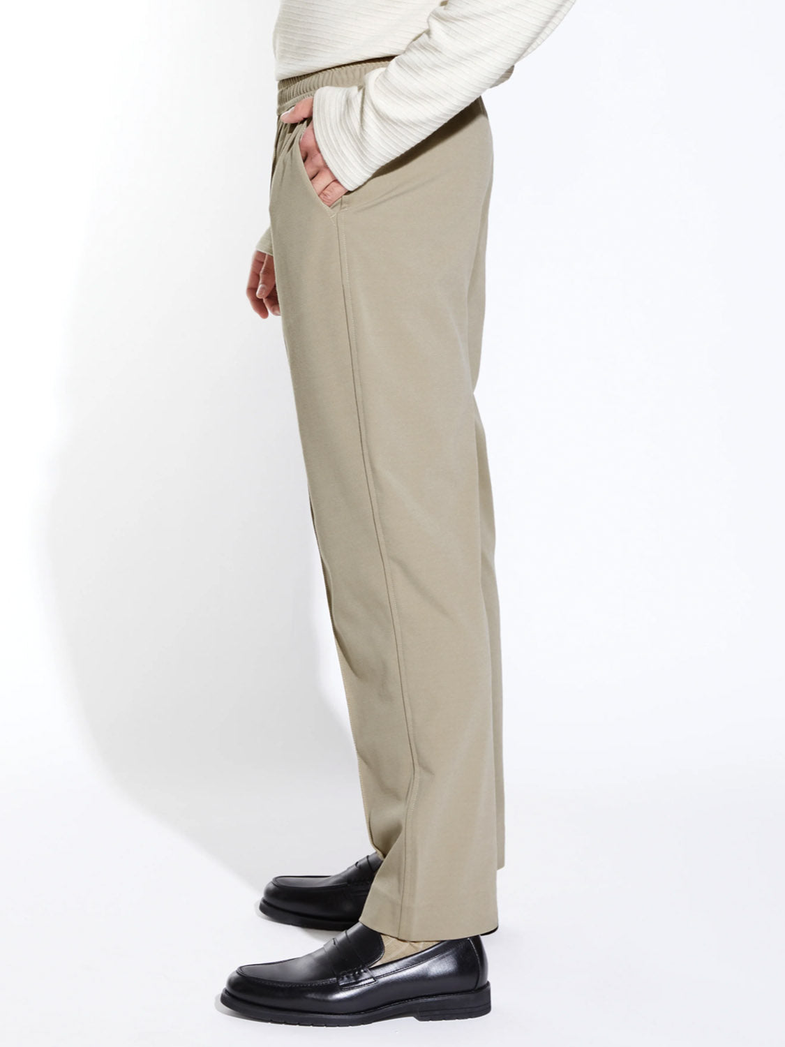 A person stands in profile against a white background, wearing the Civil Society Klien Loose Fit Dressy Trouser with a light long-sleeve top and black dress shoes, one hand in their pocket.