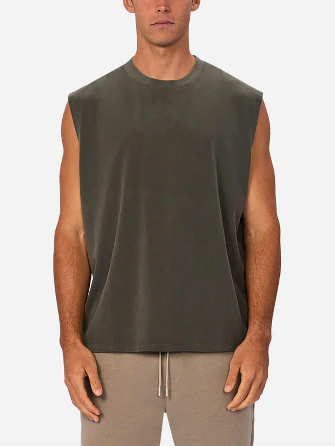 A man stands facing forward against a plain, light background wearing Industrie’s The Kosta Sleeveless Tee in dark olive green and beige drawstring shorts.