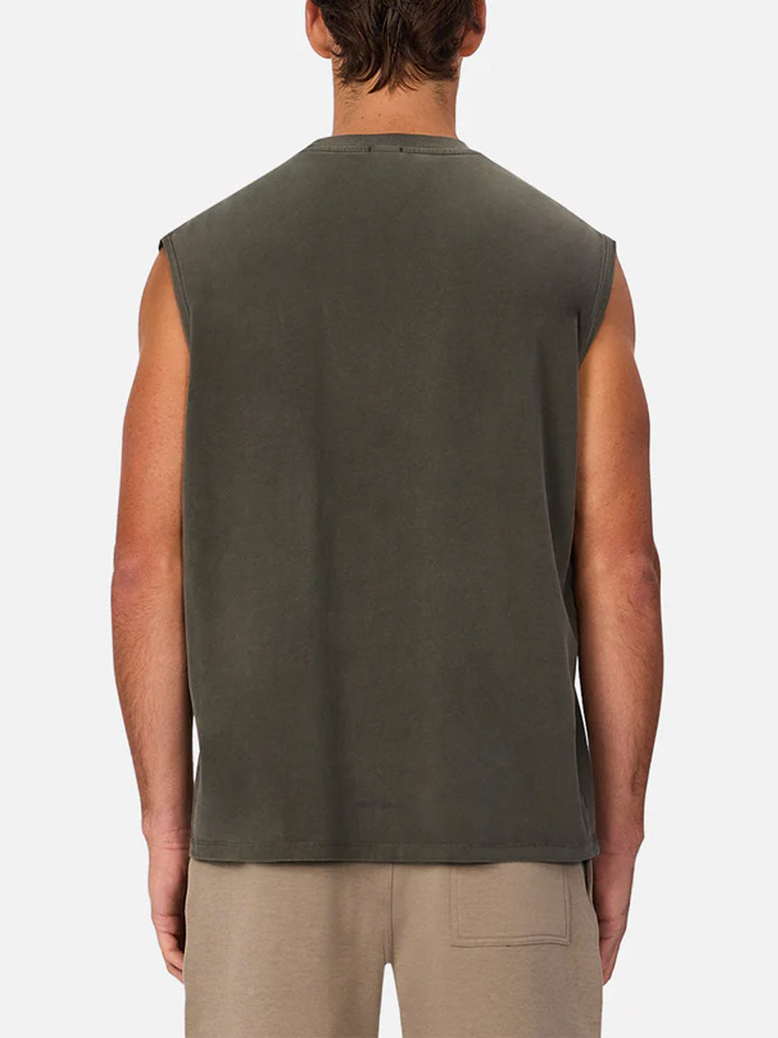A man faces away from the camera, wearing Industrie’s The Kosta Sleeveless Tee in dark green with light beige shorts, set against a plain white background.