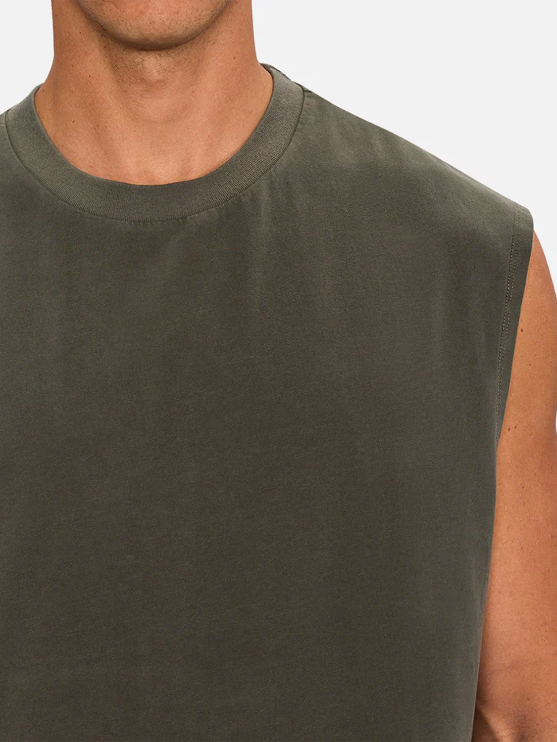 A close-up shows a person wearing The Kosta Sleeveless Tee by Industrie in dark olive green, highlighting the neck, part of the chest, and upper arm against a plain background.
