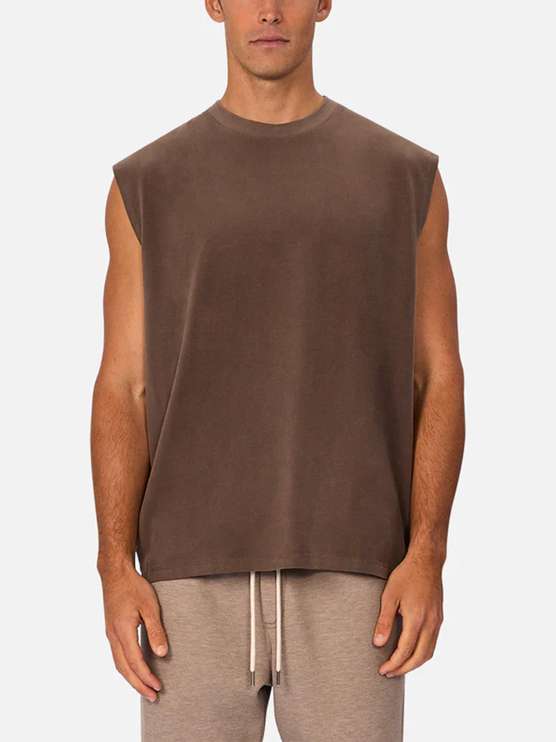 A man stands facing forward against a plain light background, wearing Industrie’s The Kosta Sleeveless Tee and light beige drawstring shorts.