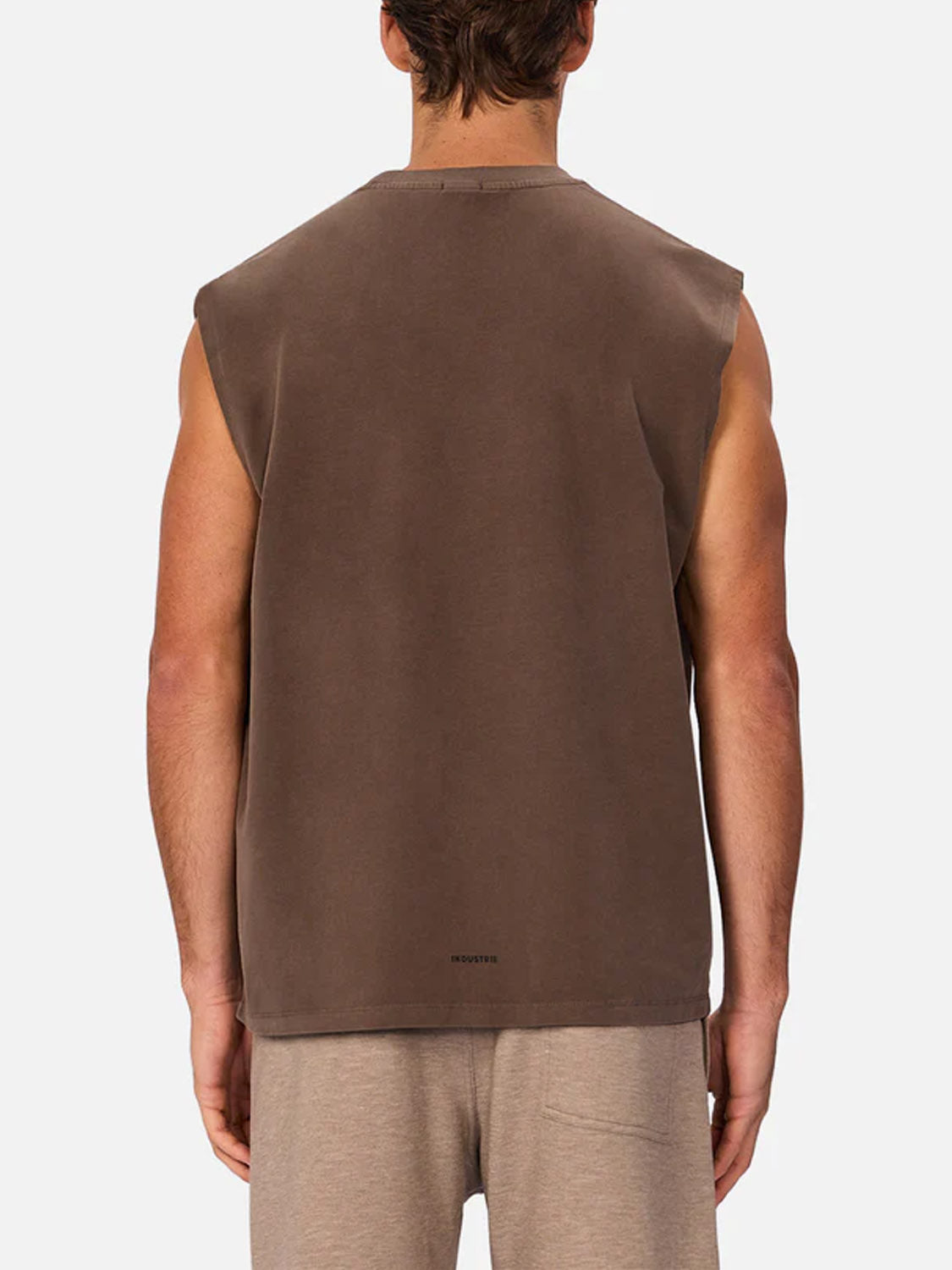 A man is seen from behind wearing the Industrie Kosta Sleeveless Tee in brown with light beige shorts, set against a plain, light background.