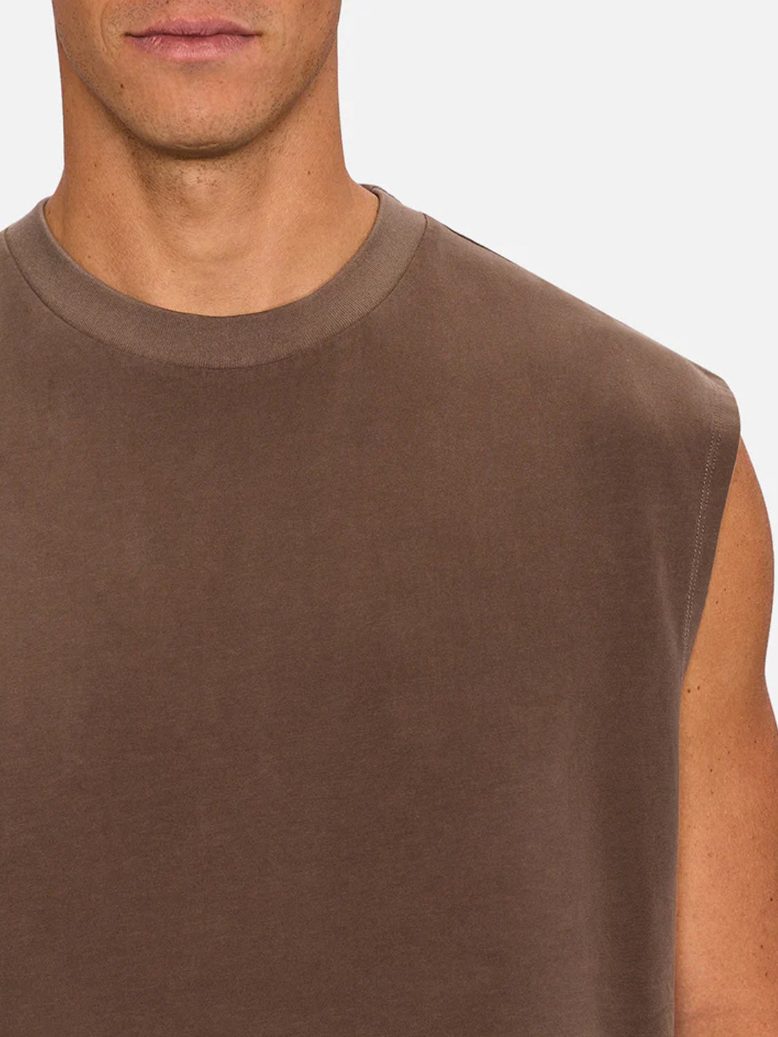 A close-up of a person wearing The Kosta Sleeveless Tee by Industrie in brown against a white background, showing only the lower half of the face, neck, and upper torso.