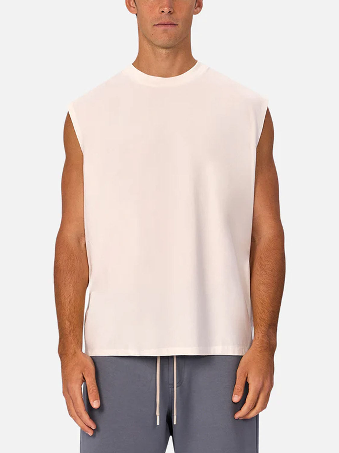 A man stands facing forward against a plain light background, wearing the Industrie Kosta Sleeveless Tee in white with gray drawstring shorts.