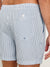 A close-up of someone wearing Rails La Brea Swim Shorts in light blue and white striped polyester seersucker, highlighting the elastic waistband, side pocket, and back pocket with a button.