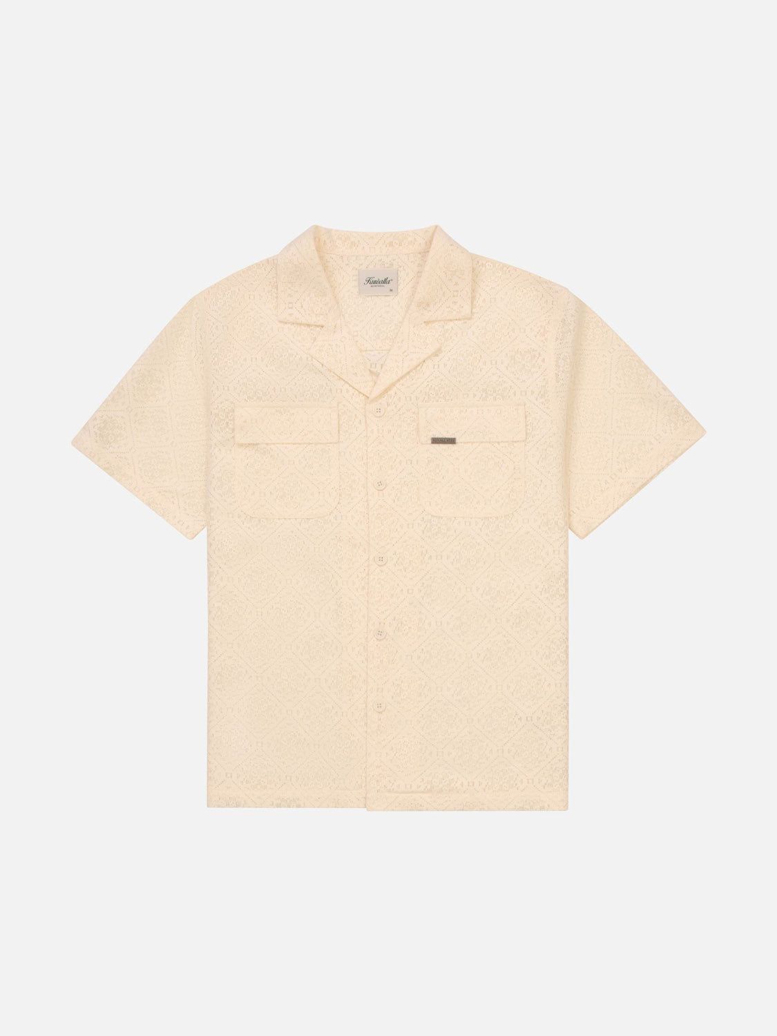 The Kuwalla Lace Yacht Shirt is a lightweight cream-colored short-sleeve button-up with a subtle textured pattern, featuring a collar, two chest pockets with a label on one. Ideal for coastal vibes and shown laid flat on a white background.