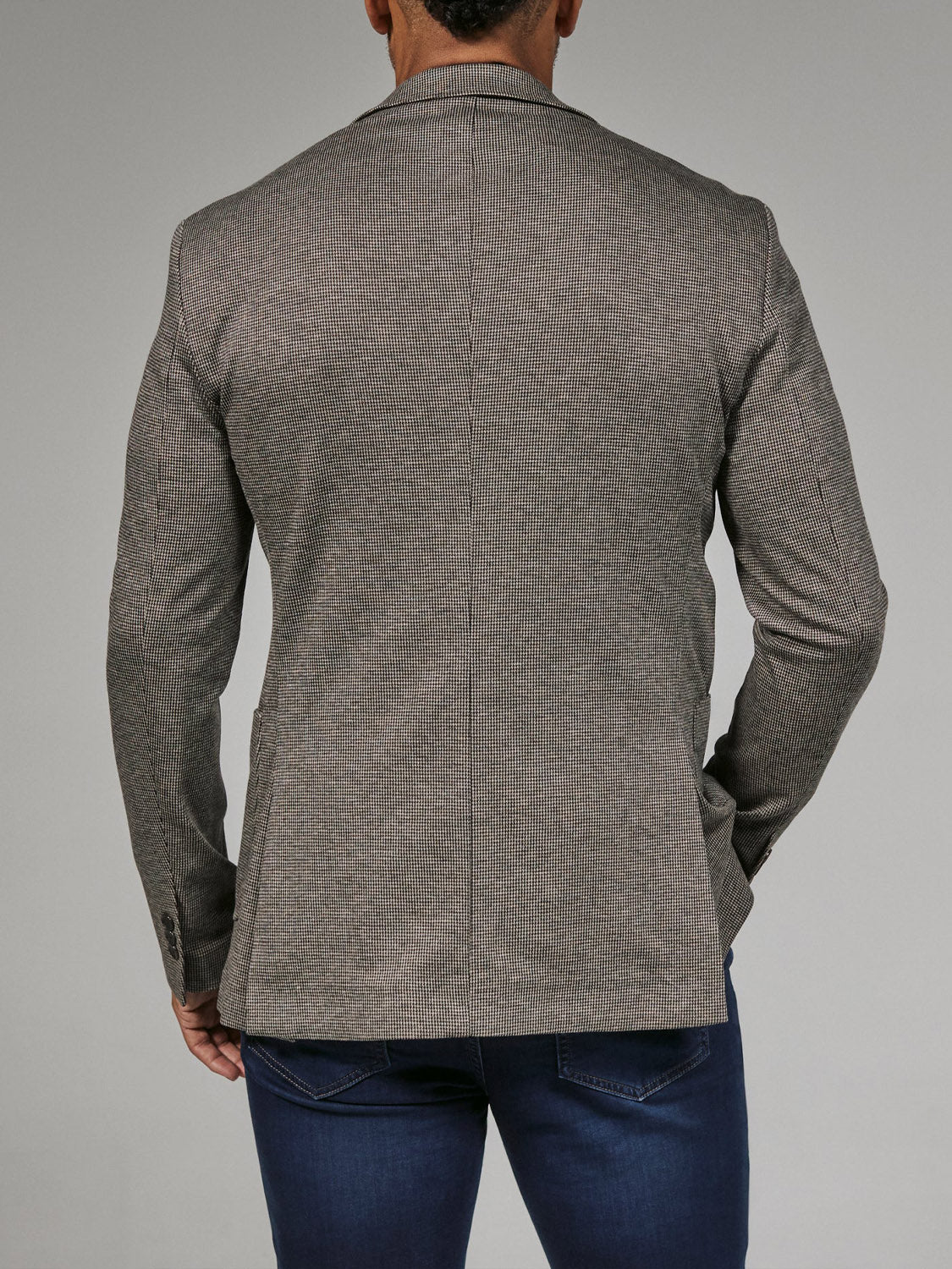 A man is seen from behind wearing the 7 Diamonds Lafayette Blazer in light brown by 7 Diamond and dark blue jeans, standing against a plain gray background.