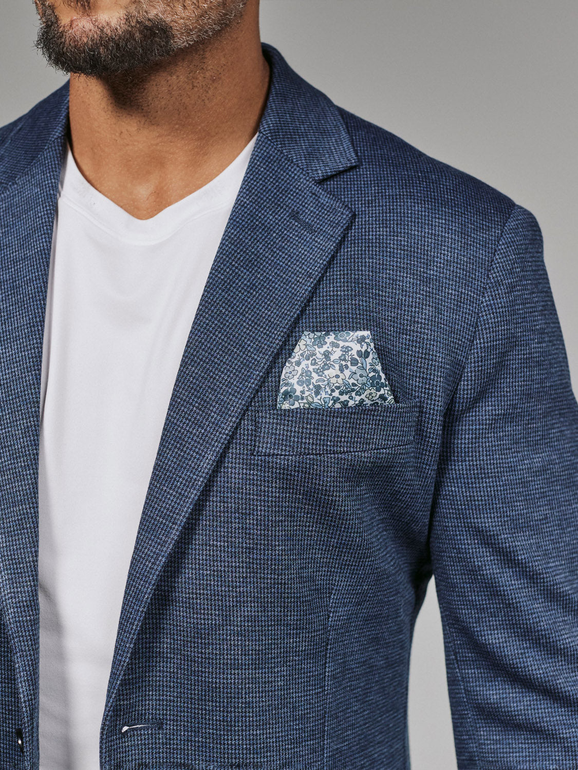 A man wears the 7 Diamonds Lafayette Blazer in blue by 7 Diamond over a white t-shirt, finishing the look with a white and blue patterned pocket square. Only his lower face and upper torso are visible.