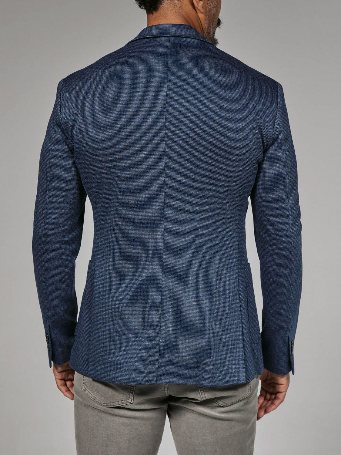 A man is seen from the back wearing the 7 Diamonds Lafayette Blazer by 7 Diamond in blue with gray pants, standing against a plain light gray background.