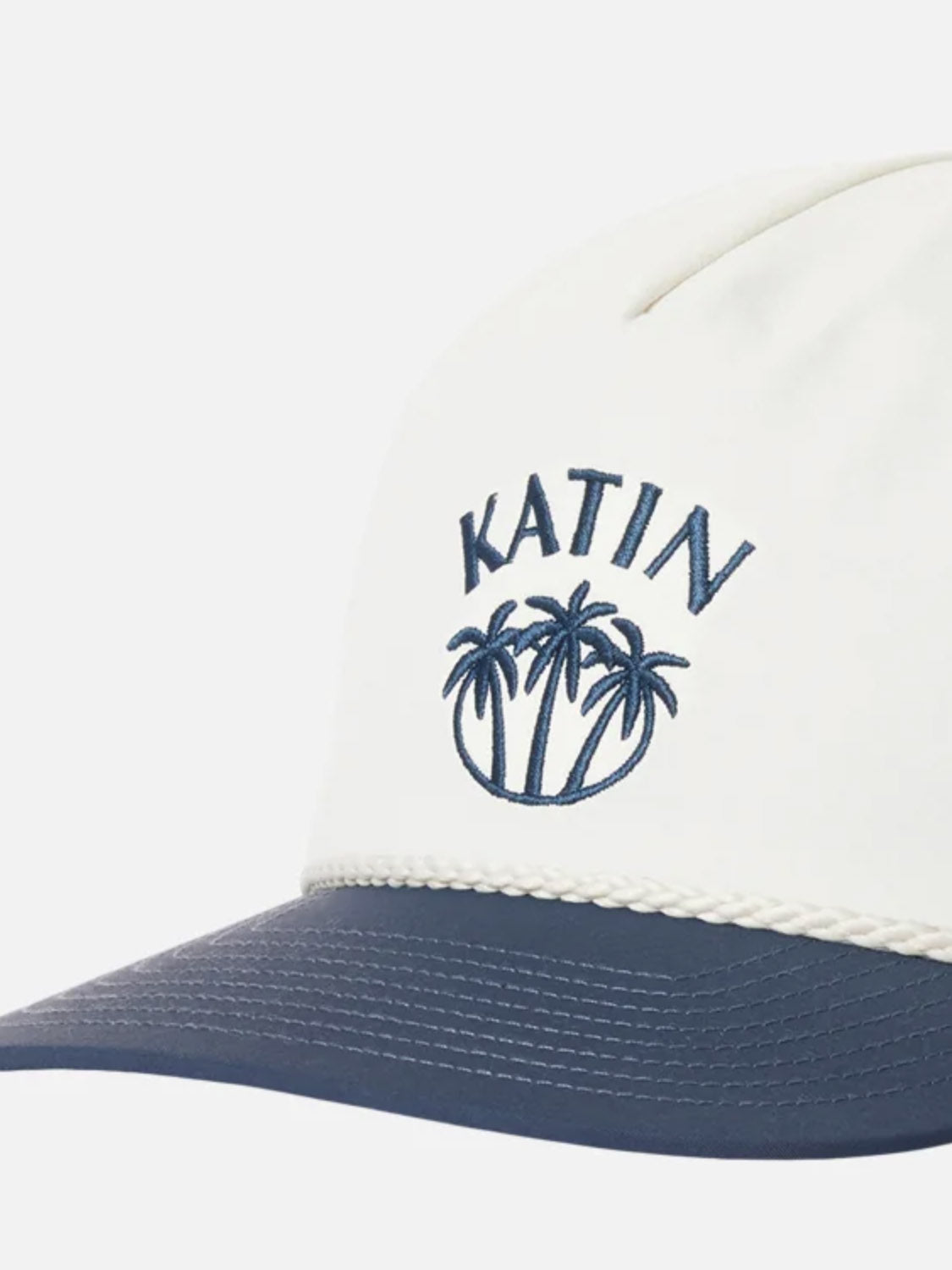 The Katin Largo Hat is a white recycled nylon hat with a dark blue brim, featuring blue "KATIN" and palm tree embroidery on the front and an adjustable snapback closure.