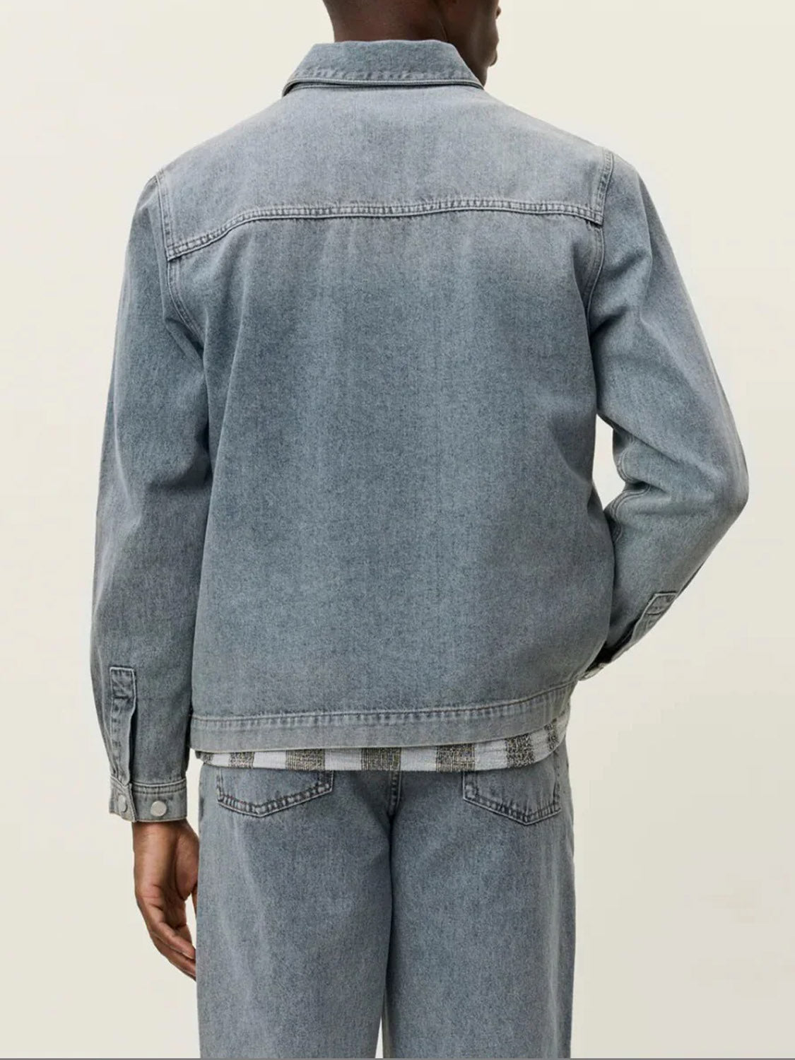 A person stands with their back to the camera, wearing the Le Deux Layton Denim Overshirt in light gray. Only the back and part of a hand are visible against a plain off-white background.