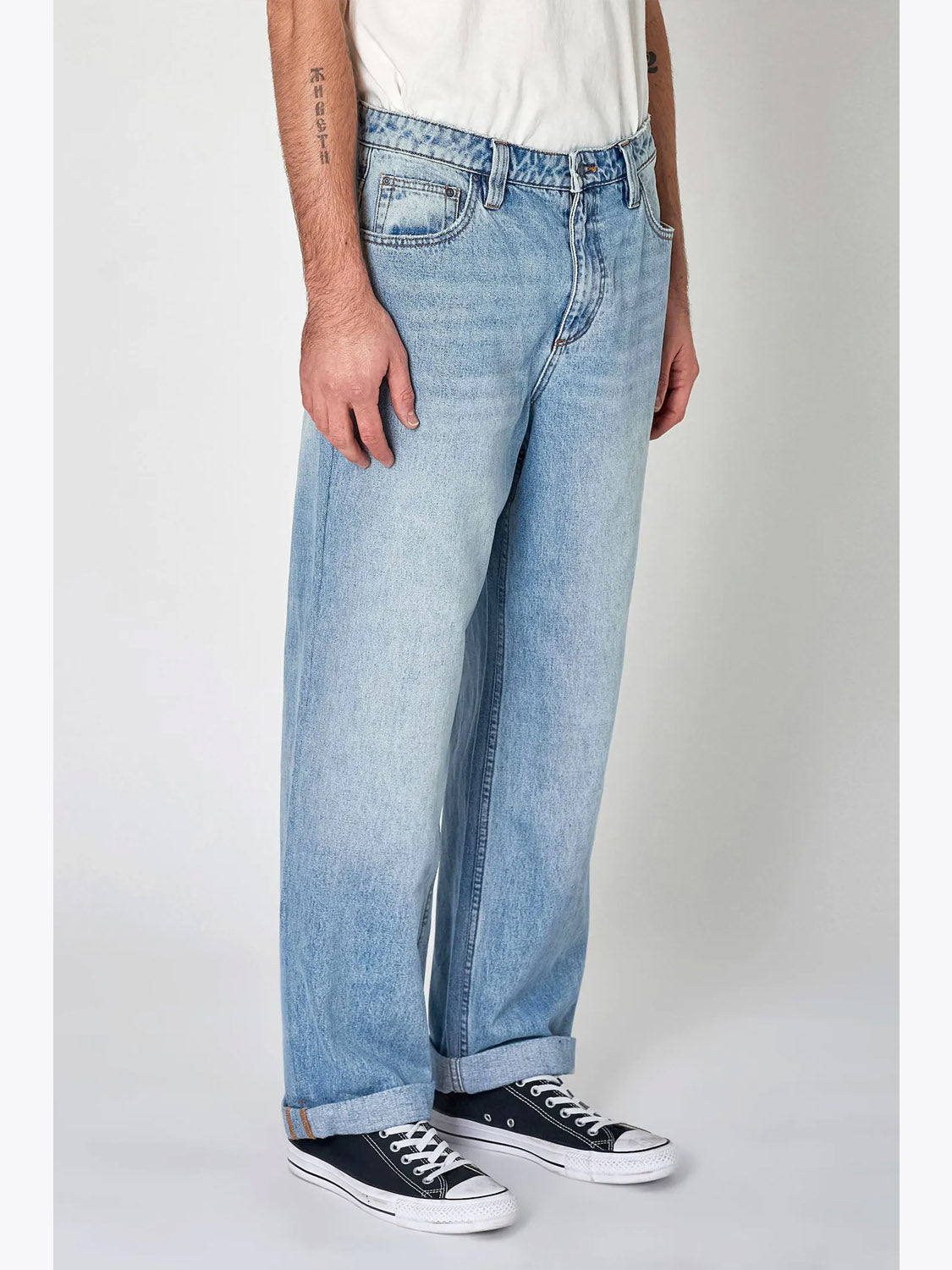 Wearing Rollas Lazy Boy Original Stone Denim jeans, a white tee, and black low-top Converse sneakers, a person stands against a plain light background with arms relaxed at their sides; only the lower torso and legs are visible.