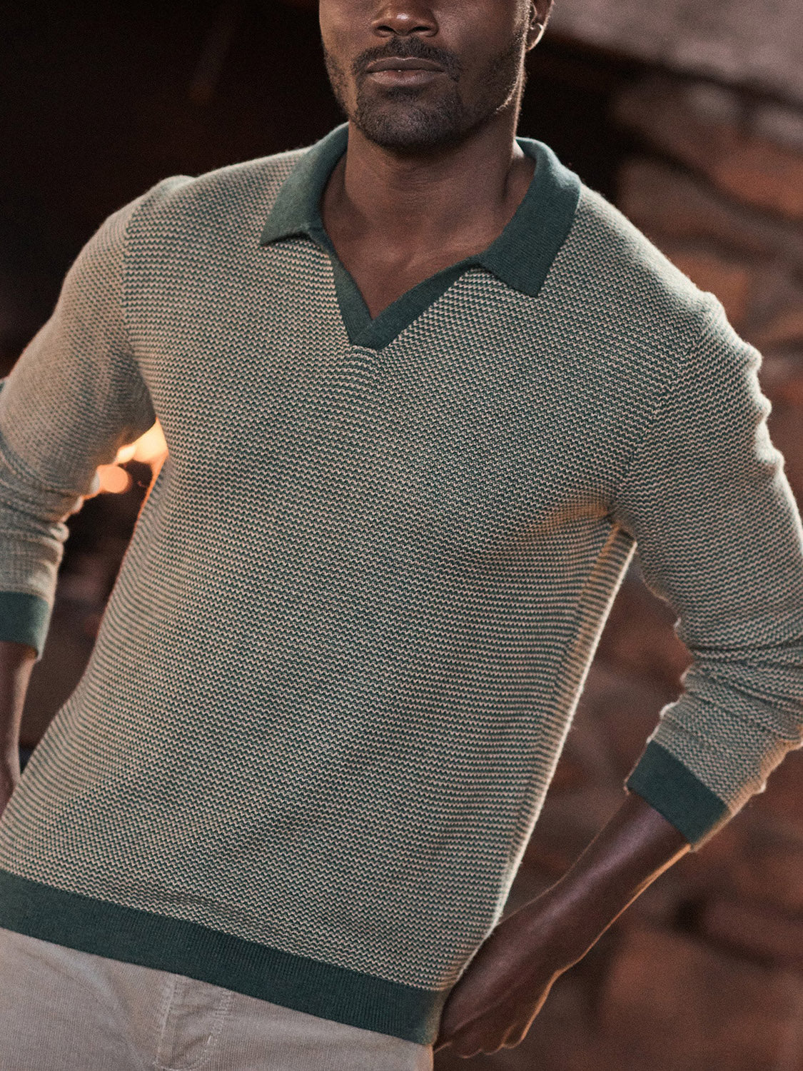 A man stands indoors wearing the Marine Layer Liam Long Sleeve Sweater Polo—a light green textured Merino wool knit with dark green Johnny collar and cuffs. His hands are on his hips, with his face partially out of frame.