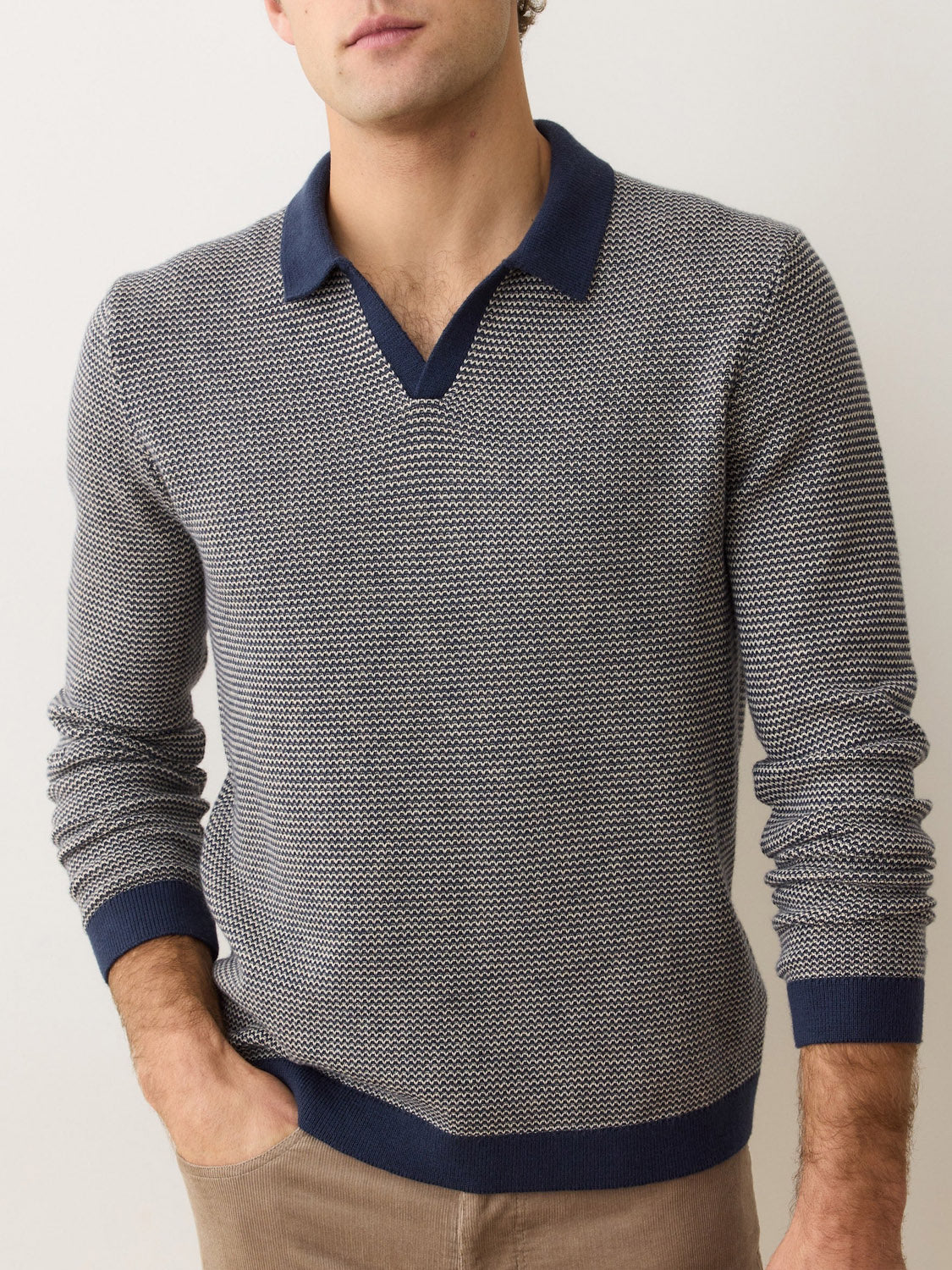 A man wearing the Marine Layer Liam Long Sleeve Sweater Polo in textured gray with a navy Johnny collar and cuffs stands against a light background, one hand in his pocket, his face partially out of frame.