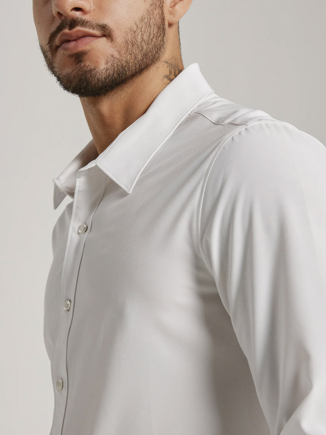 A man with a trimmed beard and mustache wears the ID Menswear Liberty 4-Way Stretch Shirt, a white long sleeve button-up with a classic collar. He is shown from the shoulders up, facing slightly to the side against a plain light background.
