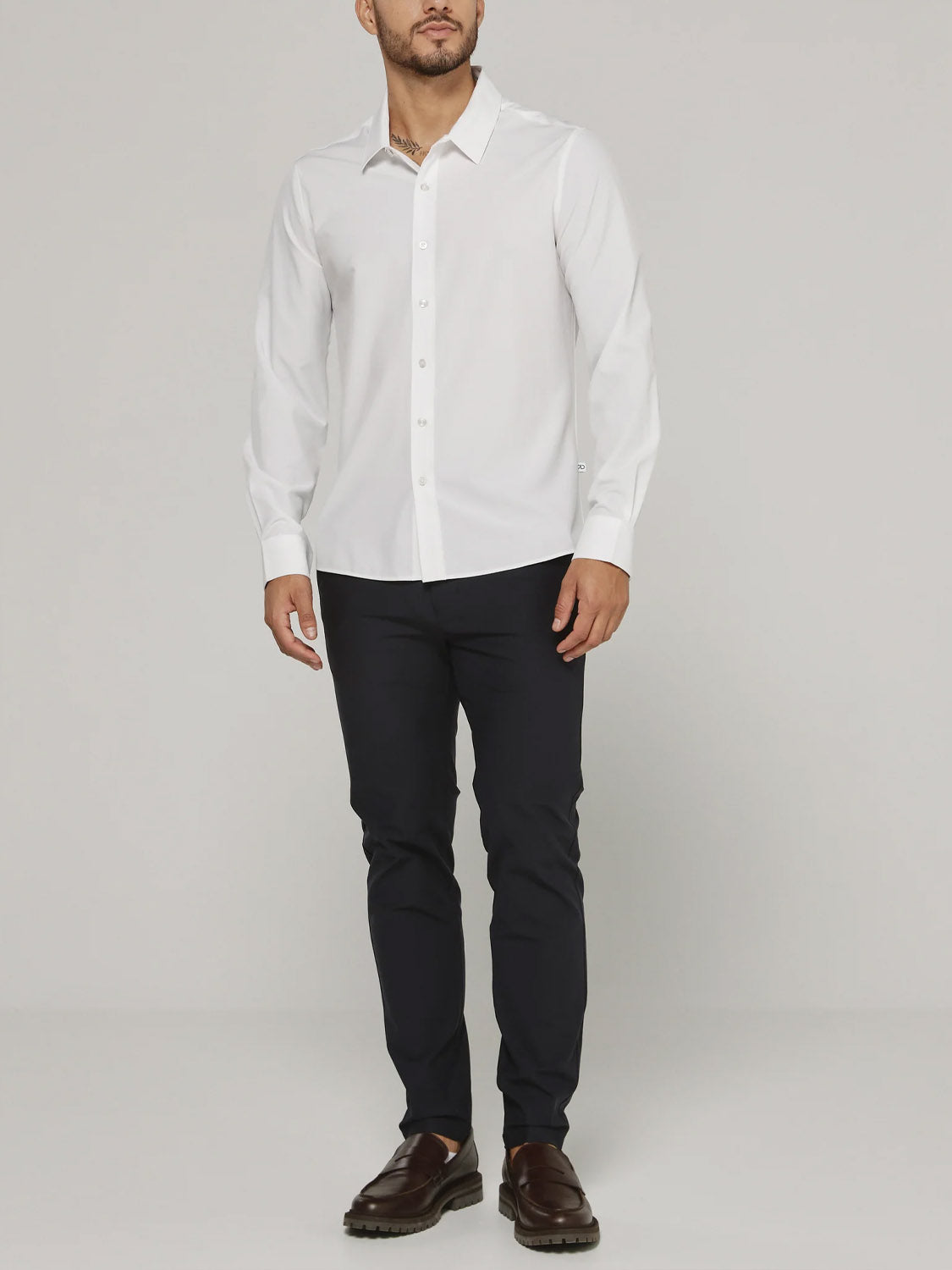 A man stands against a plain background wearing the ID Menswear Liberty 4-Way Stretch Shirt in white, paired with dark slim-fit trousers and brown loafers.