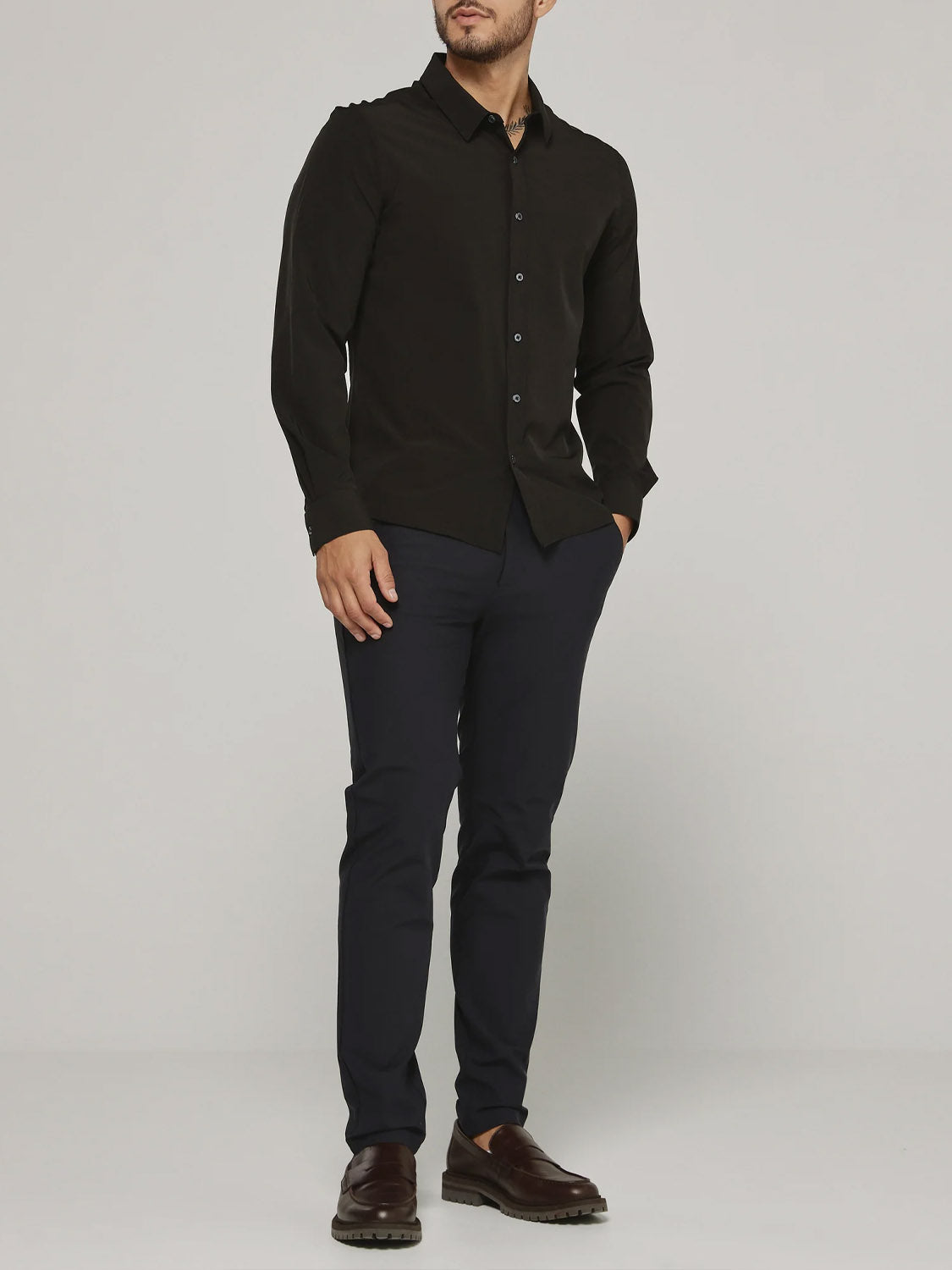 A man stands against a plain background wearing the ID Menswear Liberty 4-Way Stretch Shirt in black, paired with dark slim-fit pants and brown dress shoes, his hands in his pockets.