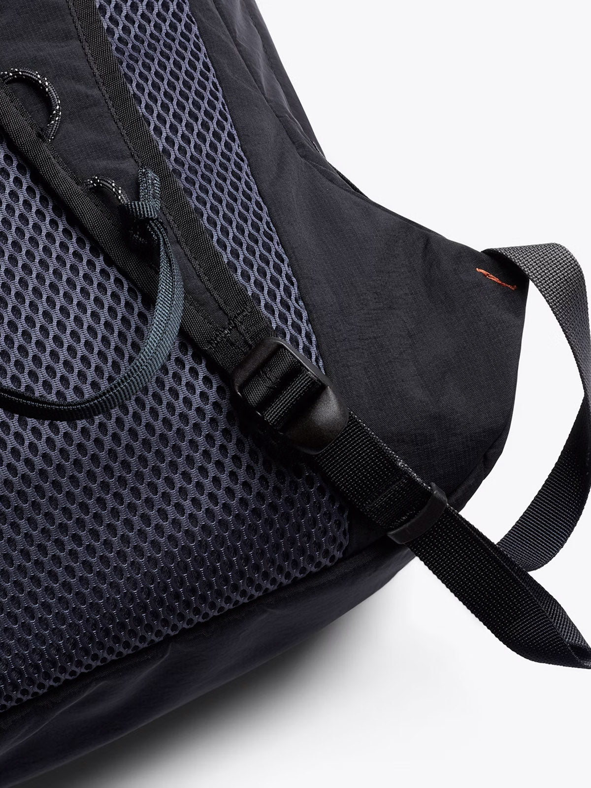 Close-up of the Bellroy Lite Daypack - 20L in black, highlighting its mesh pocket, adjustable buckle strap, and reinforced stitching, displayed against a plain light background.