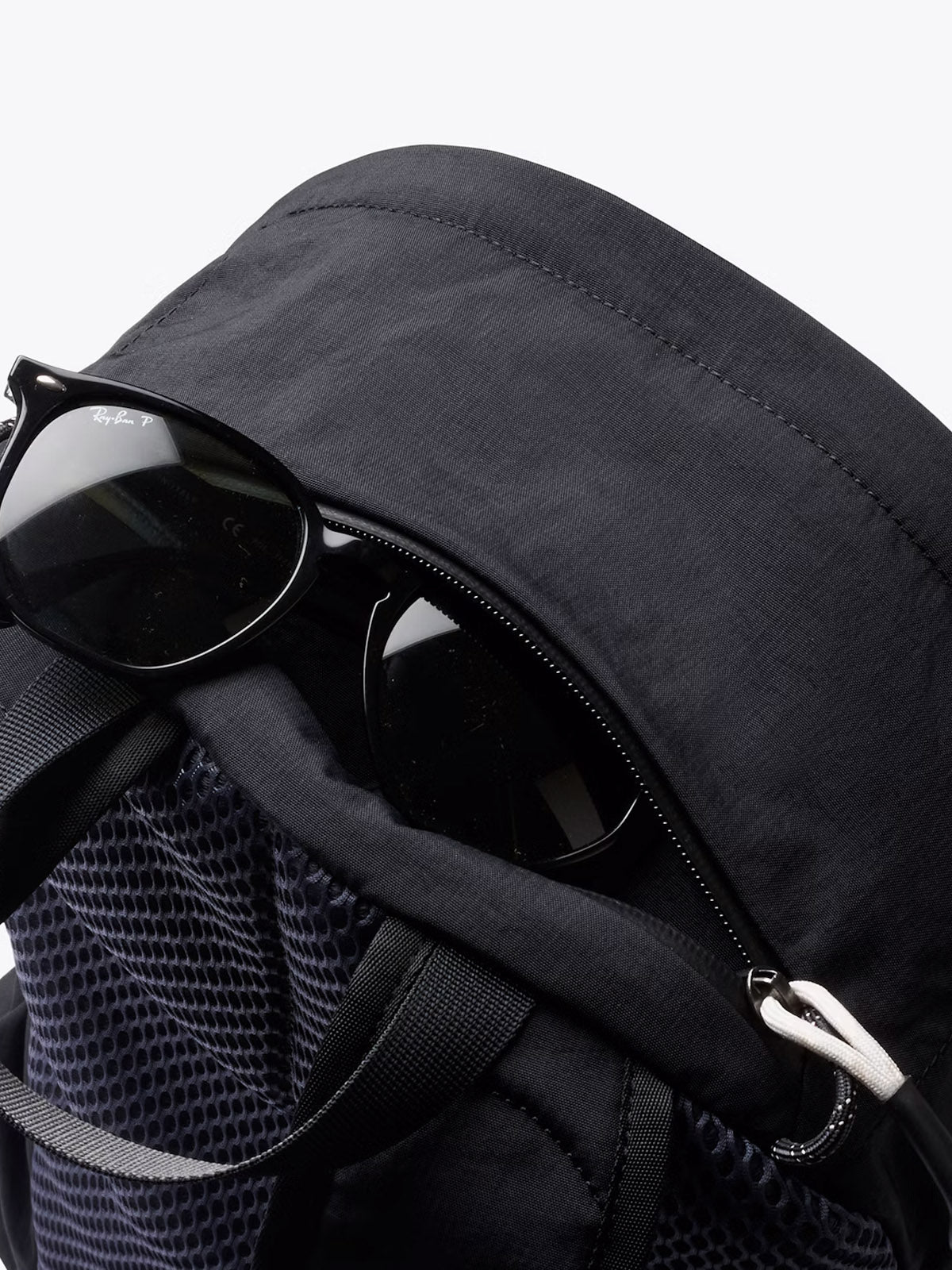 Close-up of the Bellroy Lite Daypack - 20L, showcasing its durable build and mesh details, with black sunglasses partly tucked into the top zippered pocket, set against a plain white background.