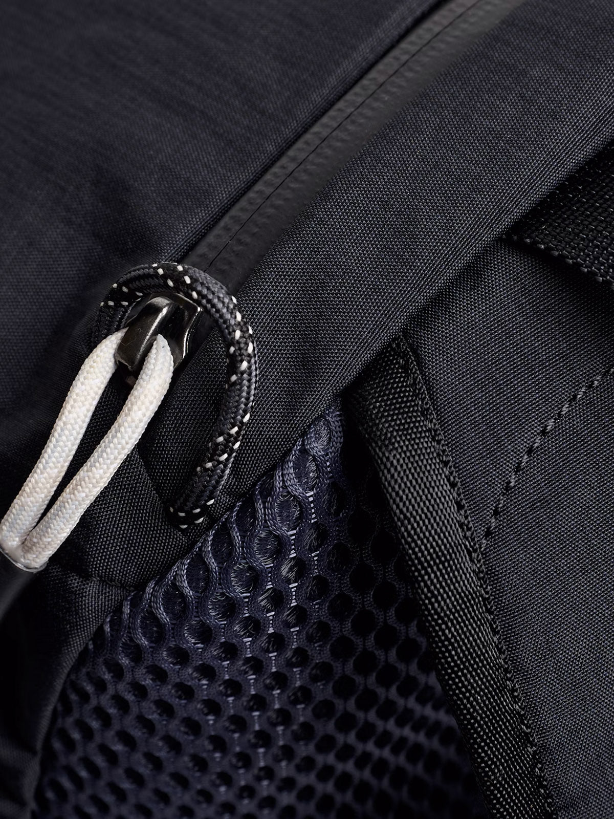 Close-up of the Bellroy Lite Daypack - 20L, featuring a zipper with a white pull cord, textured mesh pocket, and detailed stitching on the lightweight fabric.