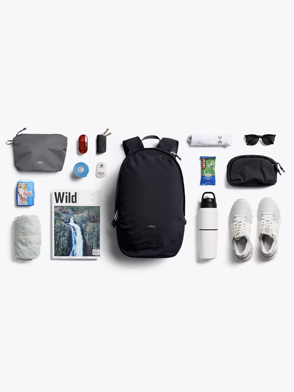 Flat lay of travel essentials featuring the Bellroy Lite Daypack - 20L, white sneakers, water bottle, sunglasses, magazine, toiletries, snacks, tech accessories, and a rolled-up shirt—all neatly arranged on a white background.