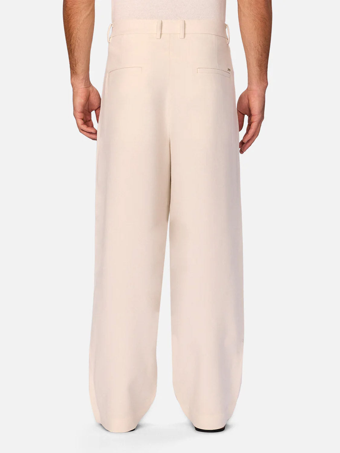 A person is seen from the back in Industrie’s The Lightweight Lusso Pant—high-waisted, cream wide leg trousers with welt back pockets and a pleated waist—cropped photo highlights their modern tailoring above the waist and below the ankles.