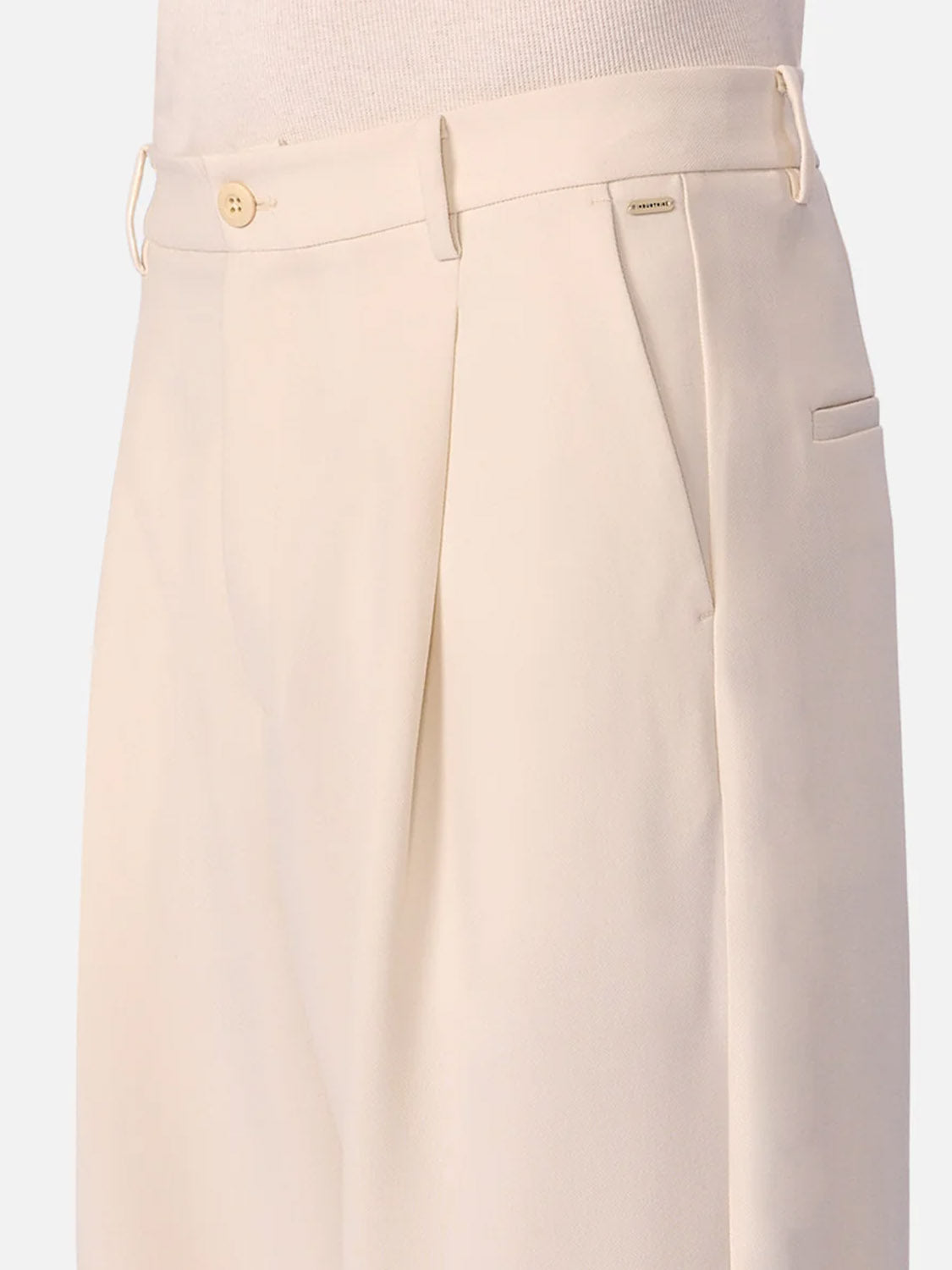 Close-up of a person wearing Industrie’s The Lightweight Lusso Pant—a high-waisted, cream pant with wide legs, pleated waist, side pockets, belt loops, and button closure. Part of a light knit shirt is also visible.