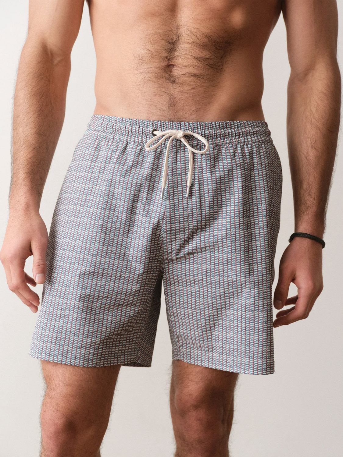 A shirtless man stands against a neutral background wearing Marine Layer Line Sport and Swim Shorts 6", featuring a drawstring waistband and patterned stretchy liner, with his arms relaxed by his sides.