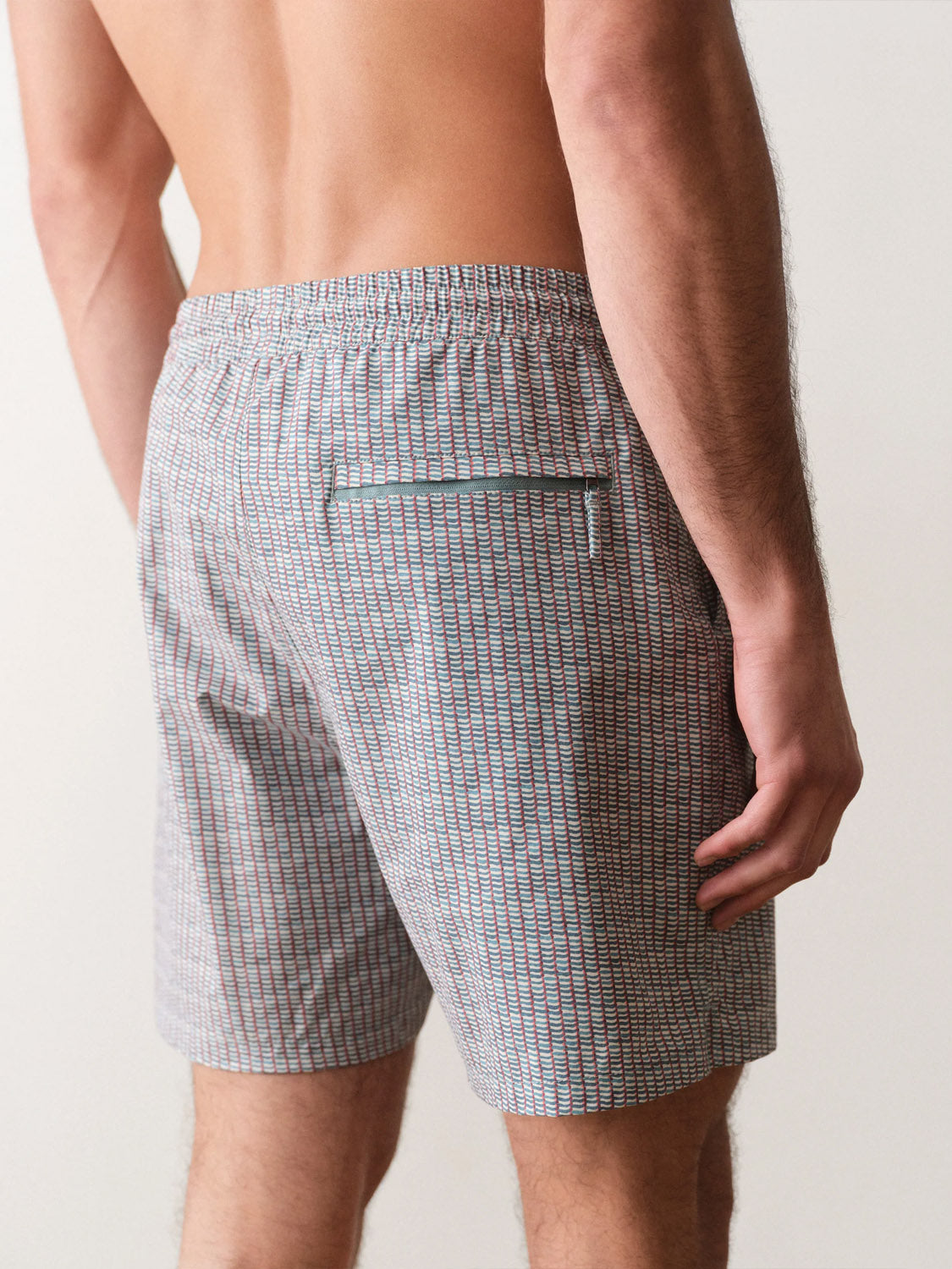 A person is seen from the back, wearing Marine Layer Lined Sport and Swim Short 6" in a light plaid pattern with a zippered back pocket. Their upper body is bare, and their hand rests at their side.