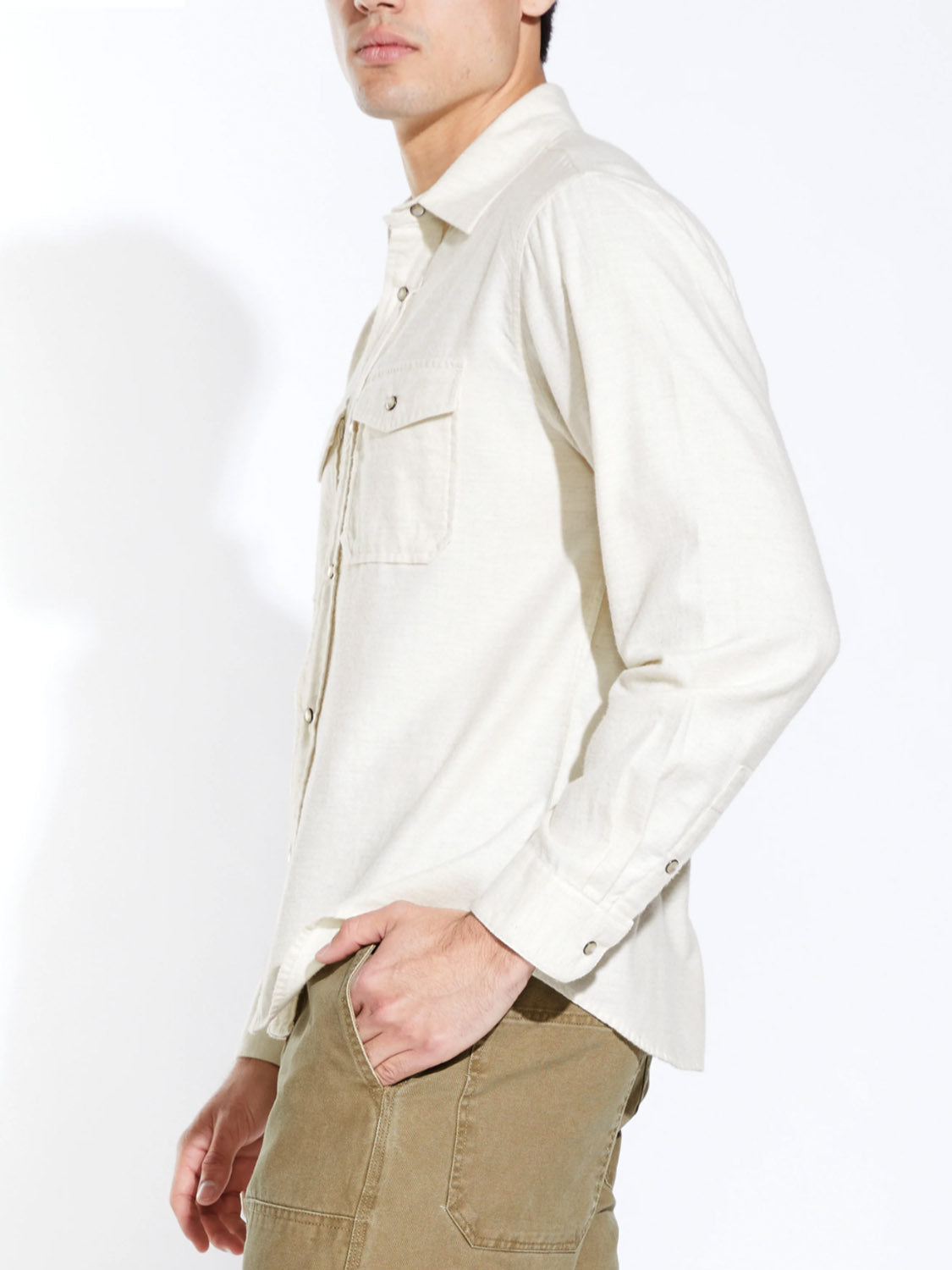A person wearing the Civil Society Linwood Relaxed Fit Western Shirt in light beige with olive green pants stands sideways, one hand in pocket, against a white background. The long-sleeve shirt features subtle faux pearl snaps. Face partially out of frame.