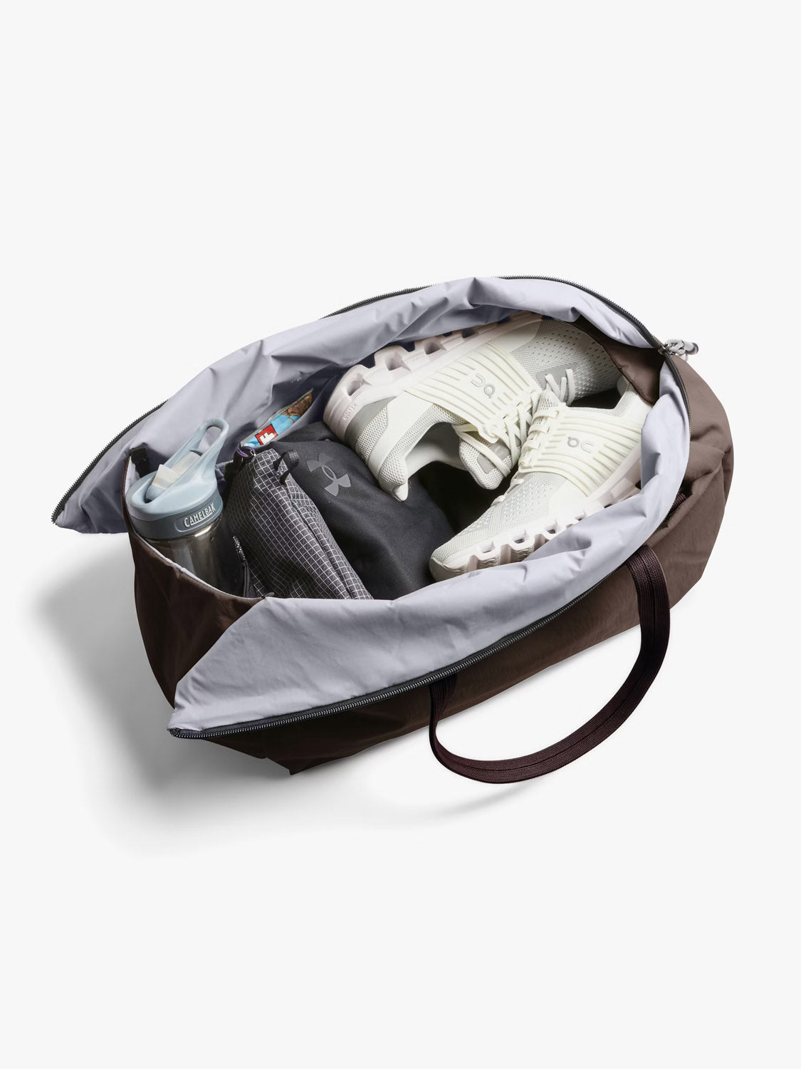 The Bellroy Lite Duffle Bag - 30L, made from recycled materials, is pictured unzipped with white athletic shoes, a black mesh bag, a clear water bottle, and socks inside—ideal for eco-conscious travelers.