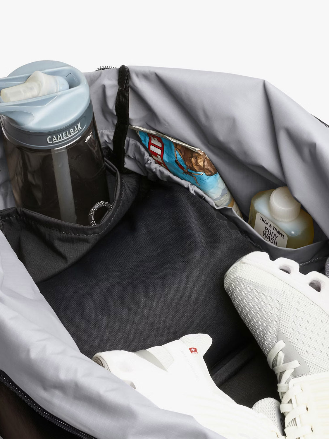 The Bellroy Lite Duffle Bag - 30L is a water-resistant gym bag packed with a water bottle, an energy bar, body wash, and white athletic shoes inside.