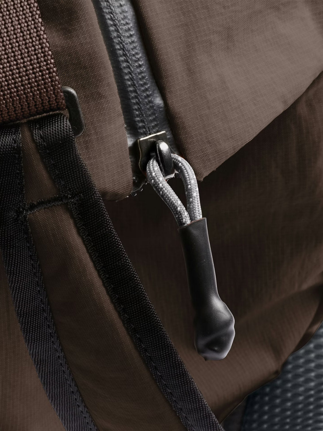 Close-up of the Bellroy Lite Duffle Bag - 30L, featuring a black zipper with a gray and black cord pull, plus sturdy black and brown straps on its brown recycled exterior.