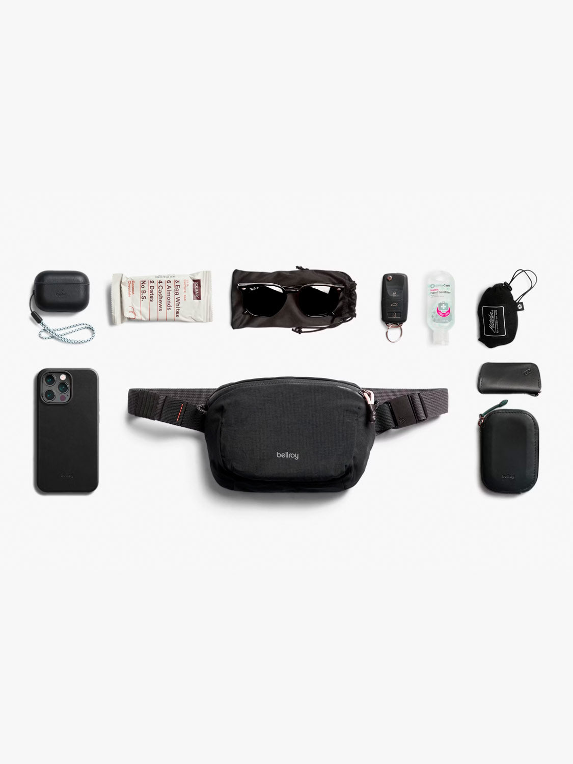 The Bellroy Lite Belt Bag, in black and water-resistant with an adjustable strap, is displayed on a white background surrounded by a smartphone, wireless earbuds, snacks, sunglasses, hand sanitizer, a car key, lip balm, pouch, and hard case.