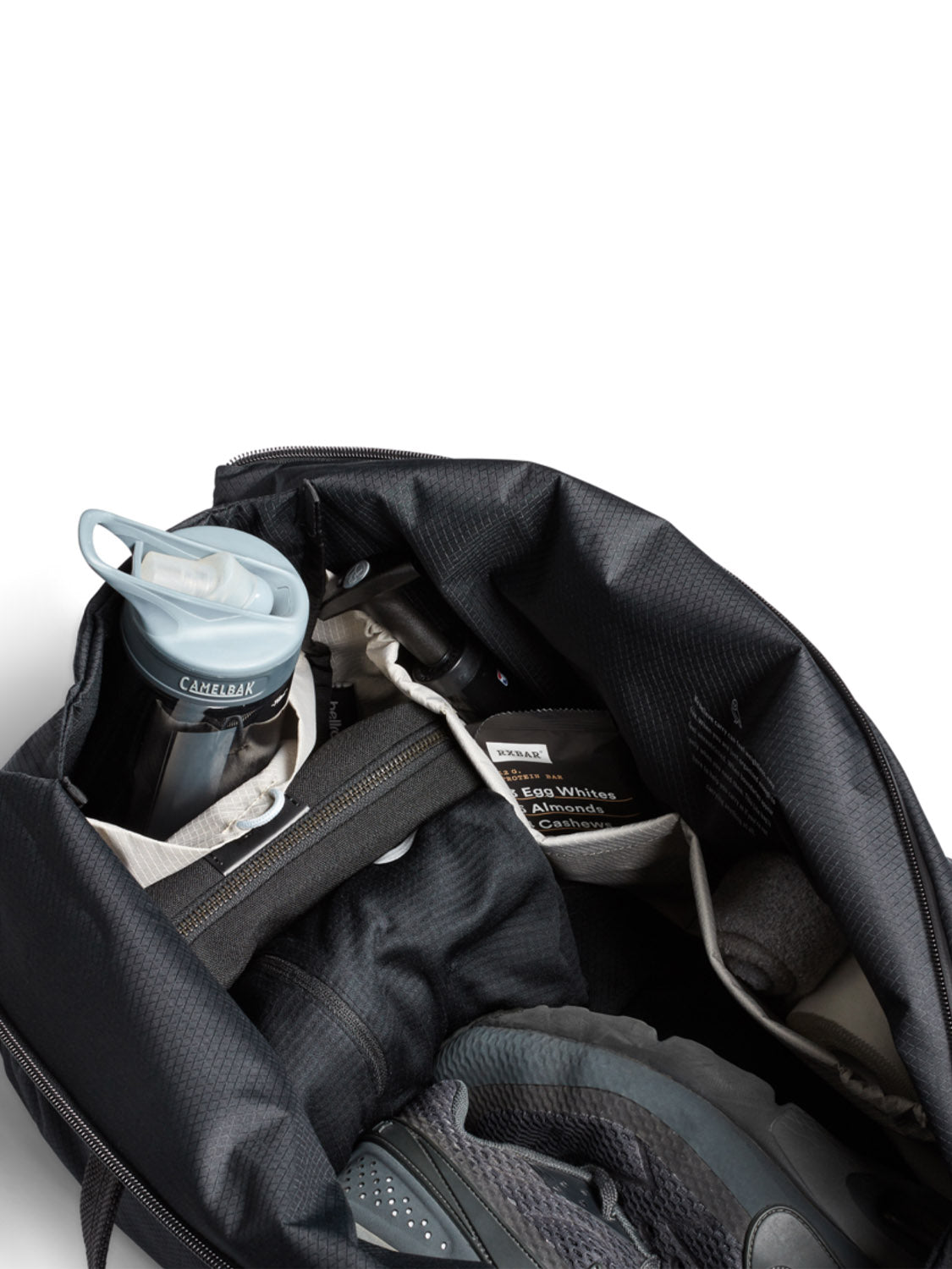 The Bellroy Lite Duffle Bag - 30L, in black, is displayed open on a white background with a blue water bottle, white towel, gray athletic shoes, and clothing neatly packed inside.
