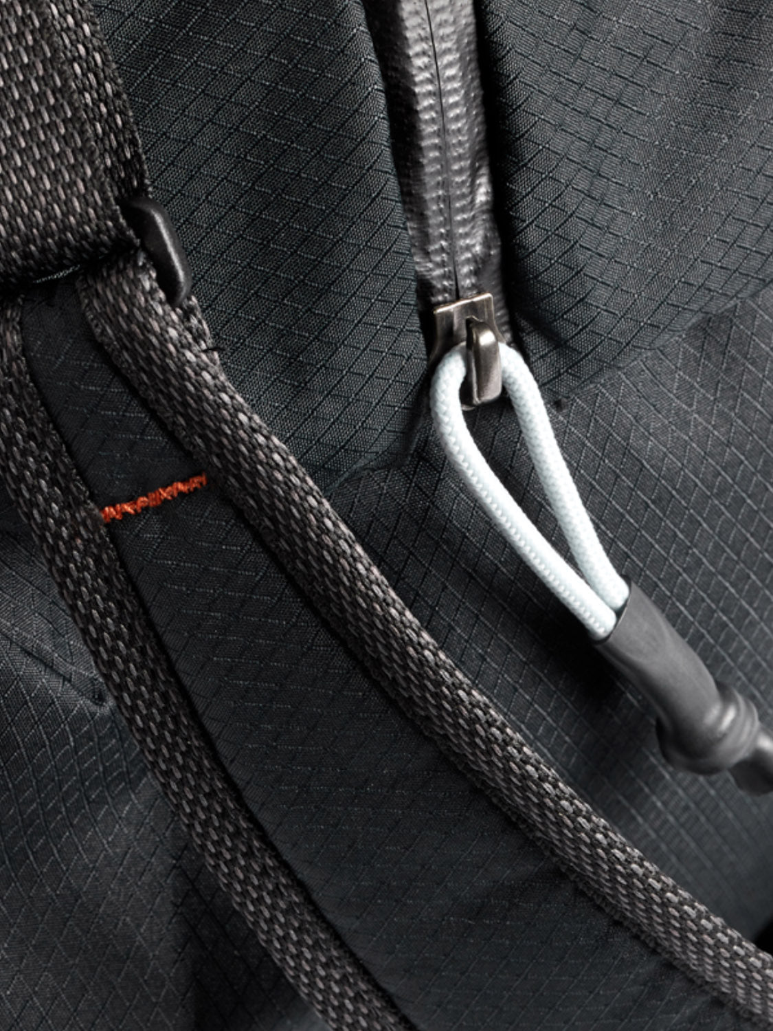 Close-up of Bellroy’s Lite Duffle Bag - 30L: features a black, textured lightweight fabric with a zipper and grey cord pull, black strap, and subtle orange stitching detail.