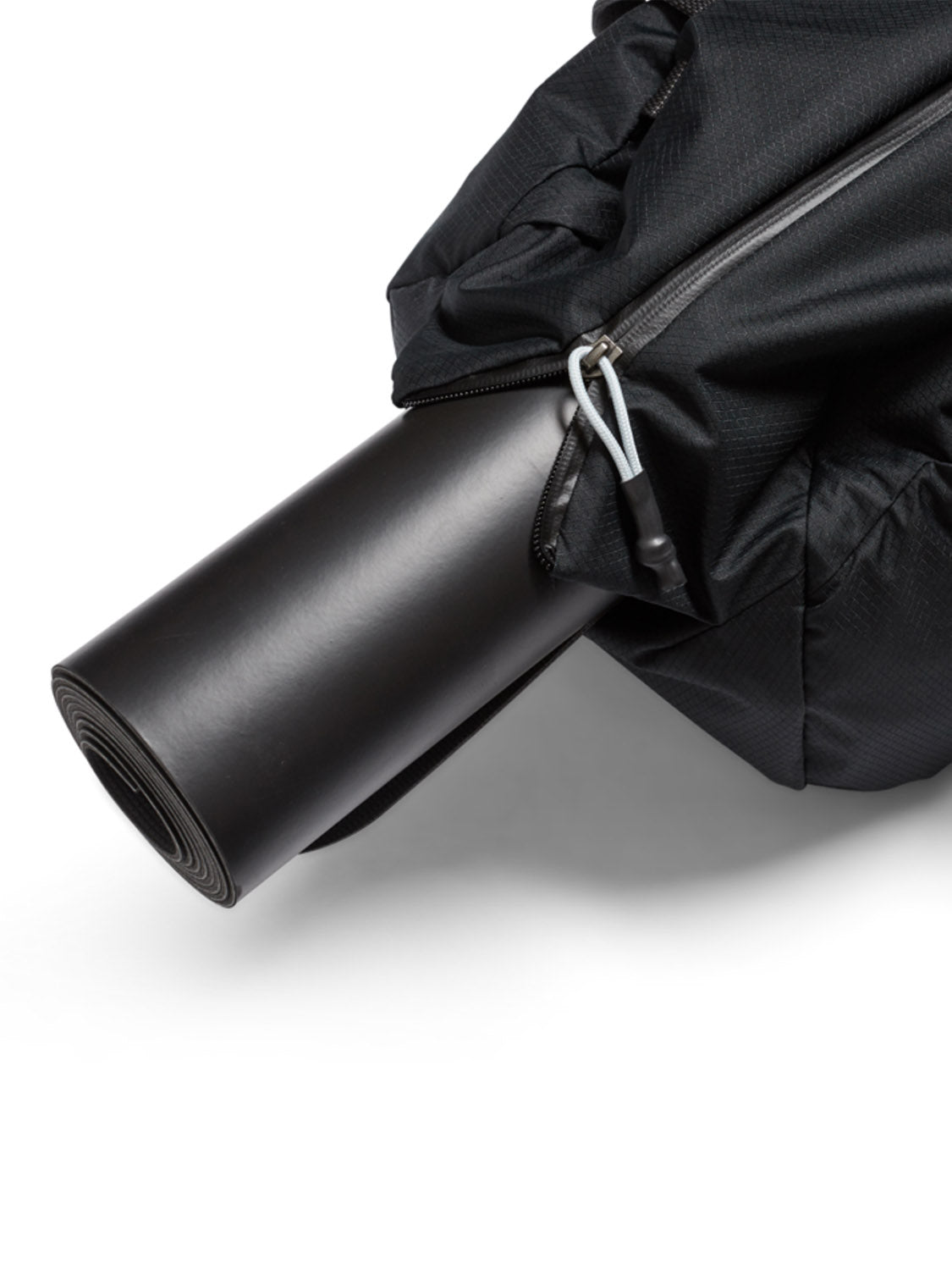A close-up of a rolled black yoga mat partially tucked into the side pocket of the Bellroy Lite Duffle Bag - 30L, a sleek, water-resistant gym bag with a zipper, shown against a white background.