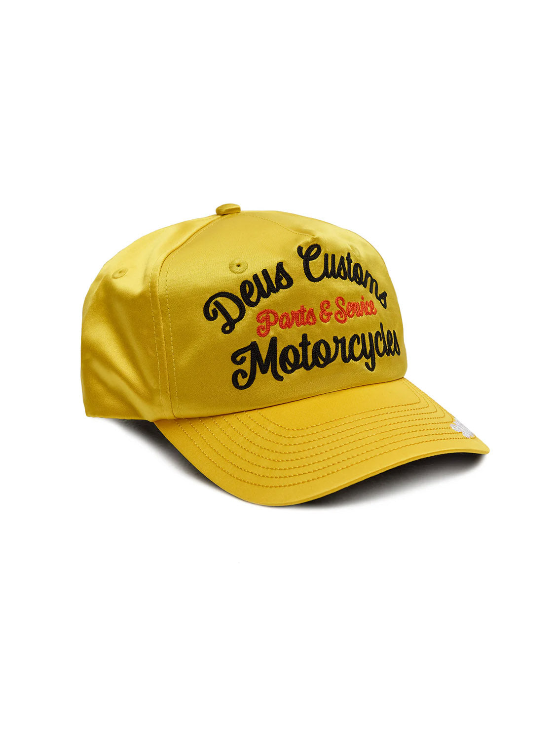 The Deus Lota Trucker is a yellow deep fit hat with black and red "Deus Custom Motorcycles Parts & Service" chainstitch embroidery on the front, a curved brim, satin fabrication, and visible stitching details.